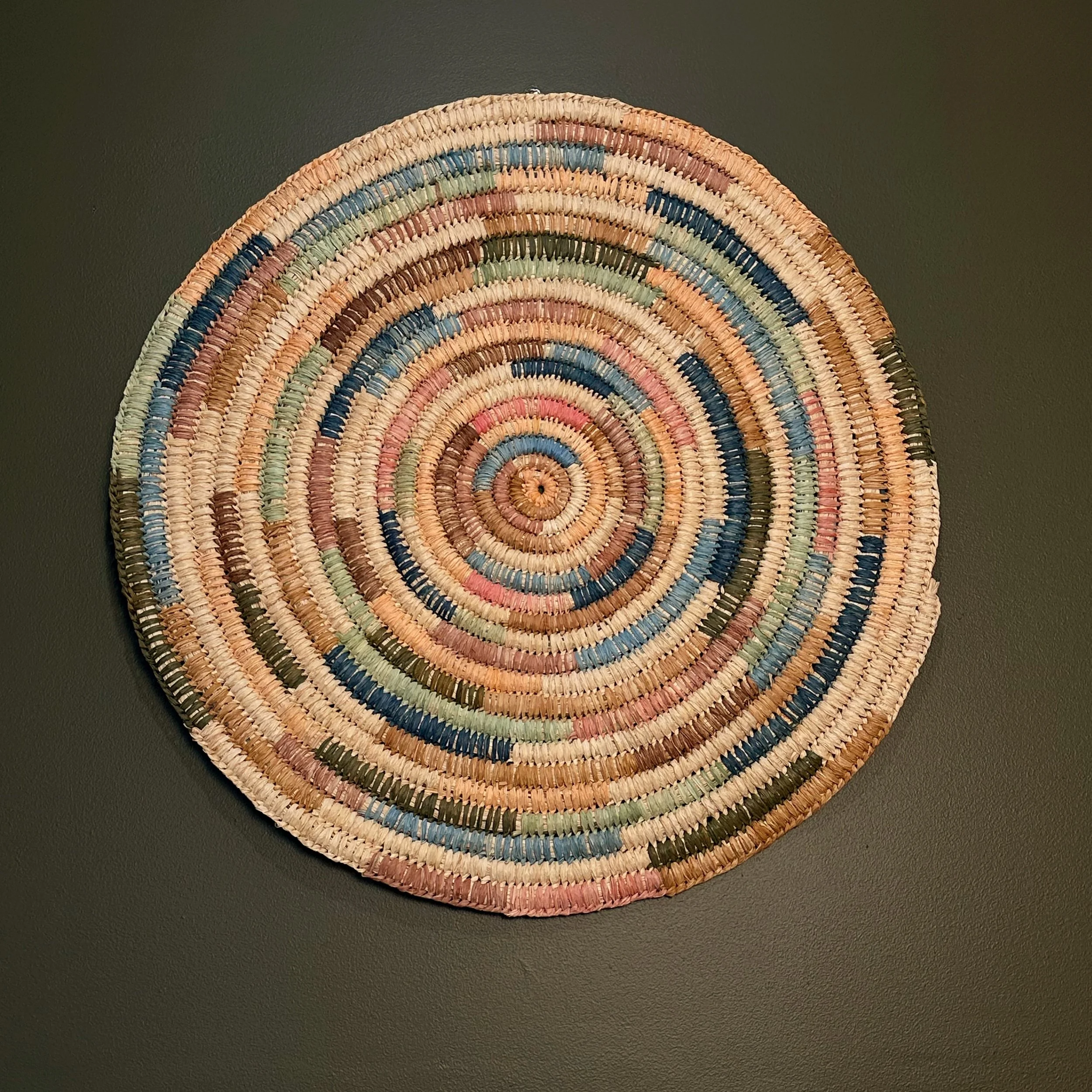 Colorful circular woven basket or mat on a dark wall.