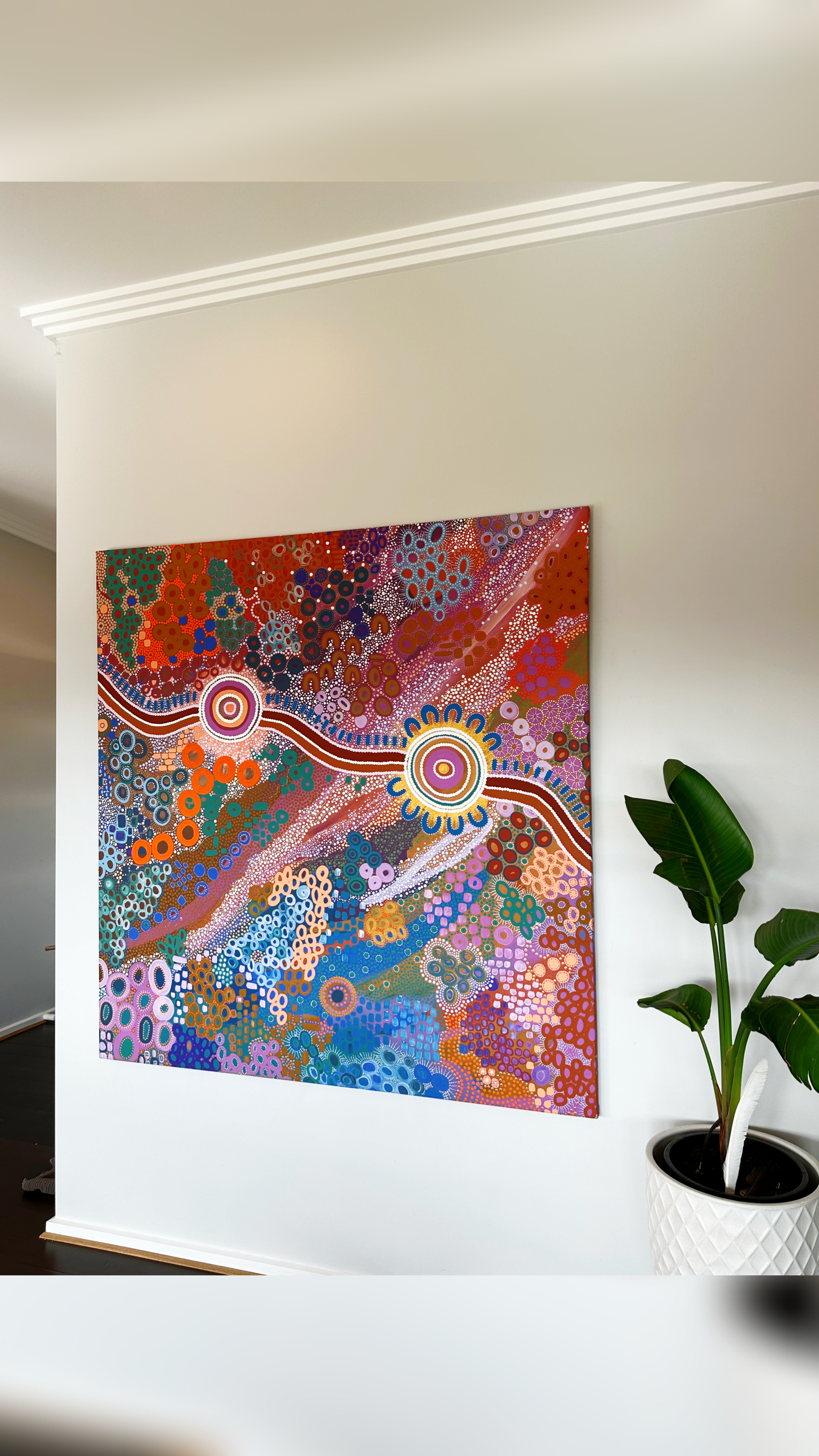 Abstract colorful dot painting on wall next to green potted plant in white planter.