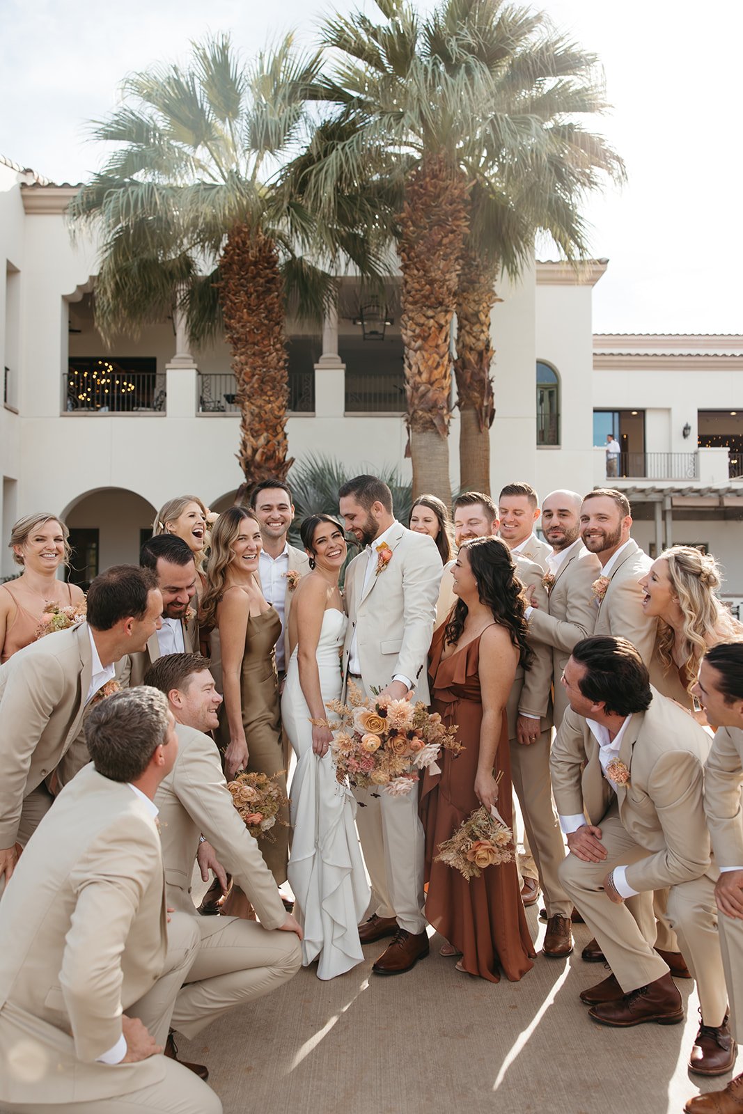  Candid moment of the bride and groom surrounded by their wedding party, laughing together outdoors at La Quinta Resort. 