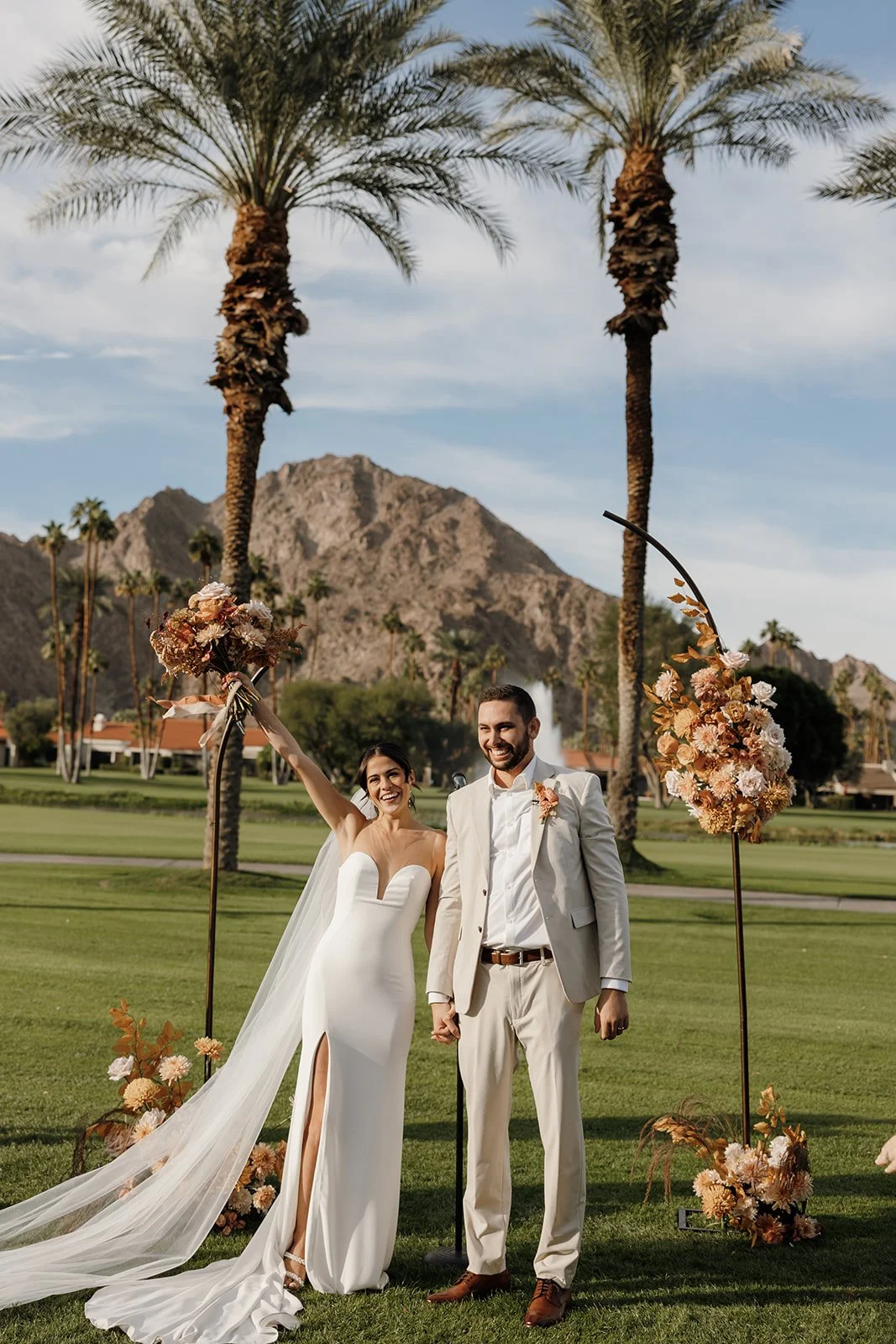  Bride raising her bouquet in celebration beside the groom during their La Quinta Resort wedding ceremony recessional. 