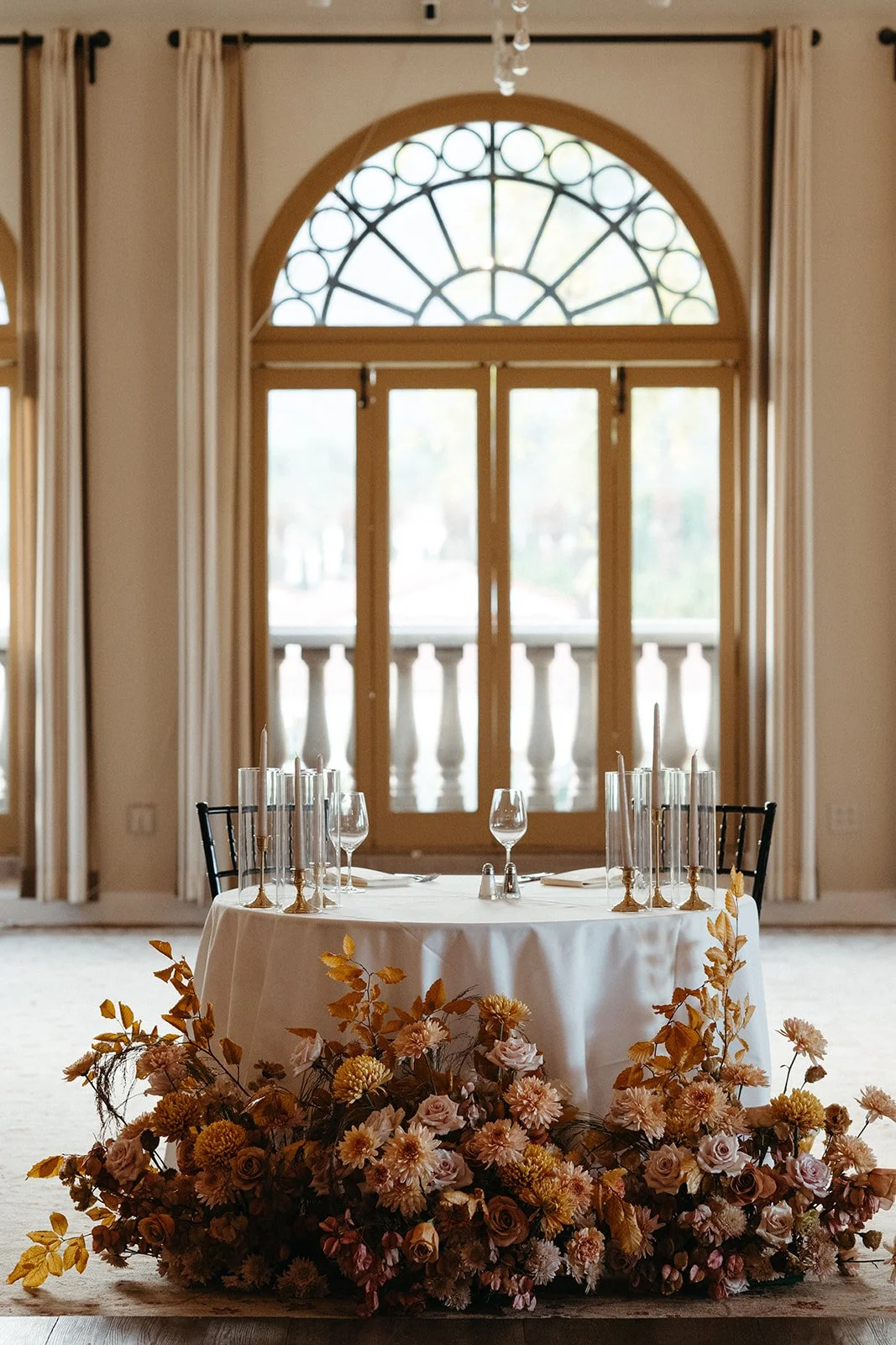  Romantic sweetheart table with a lush foam-free floral installation in warm blush and caramel tones beneath arched windows at La Quinta Resort. 