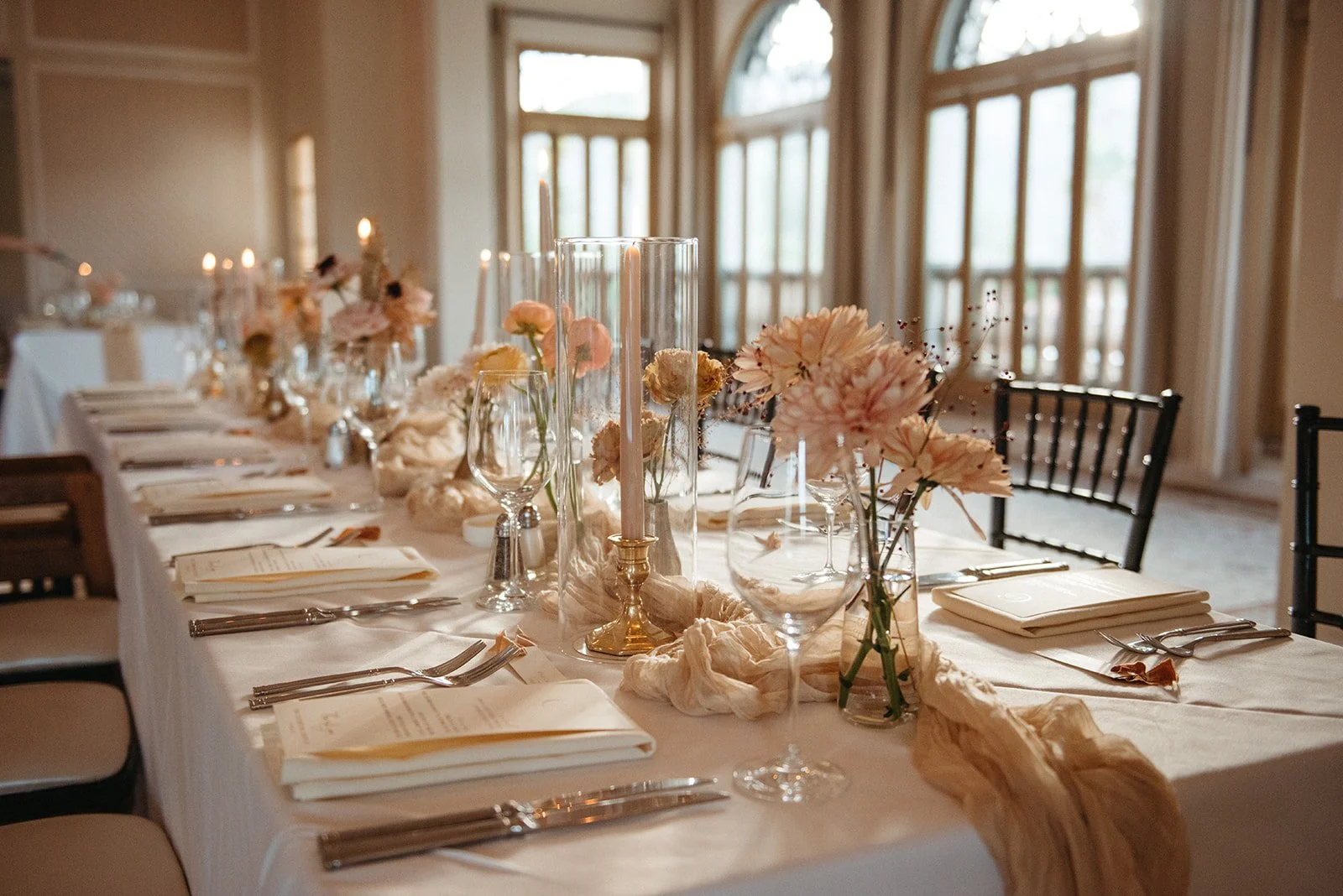  Long reception table styled with flowing neutral linens, glass cylinder candles, and delicate bud vase florals in warm autumn tones at La Quinta Resort. 