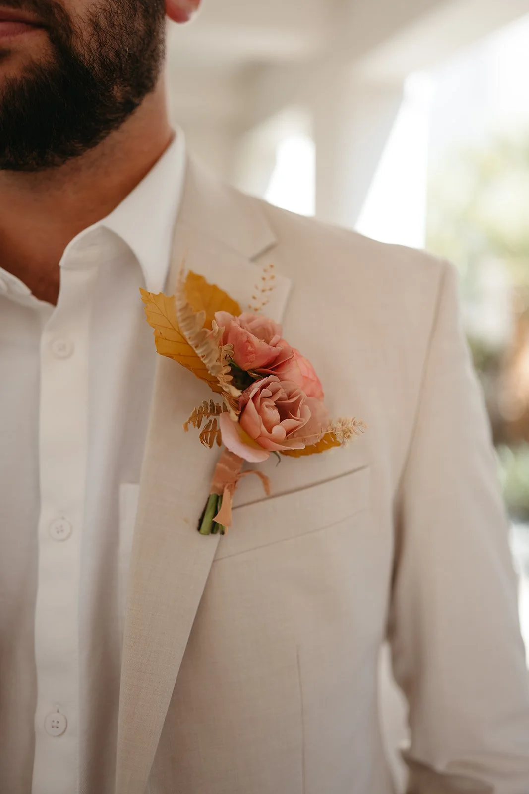  Groom wearing a cream suit with a soft blush and peach rose boutonniere accented with warm autumn foliage at a November wedding at La Quinta Resort.t 
