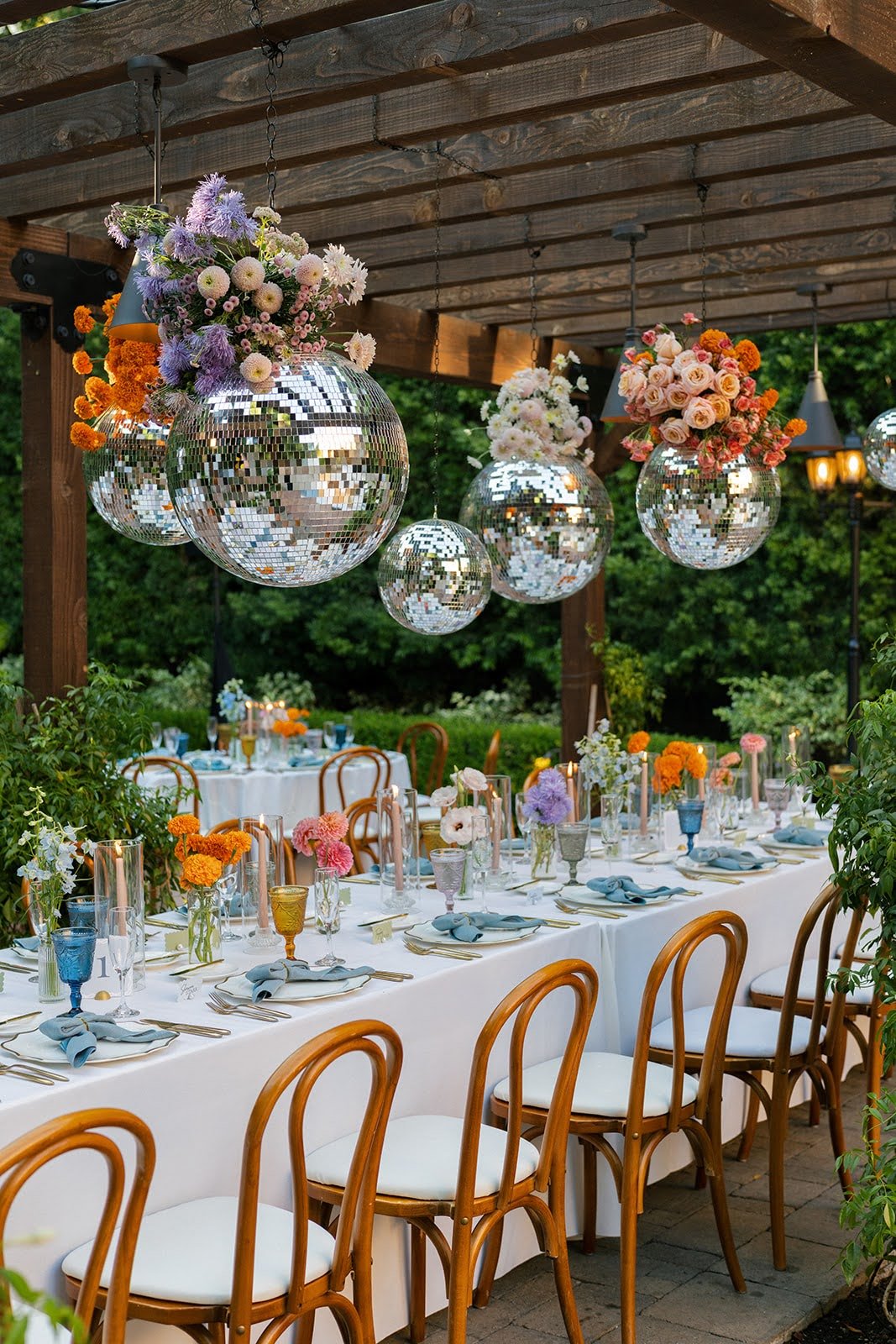 Hanging disco balls filled with flowers above outdoor reception tables with bud vases.