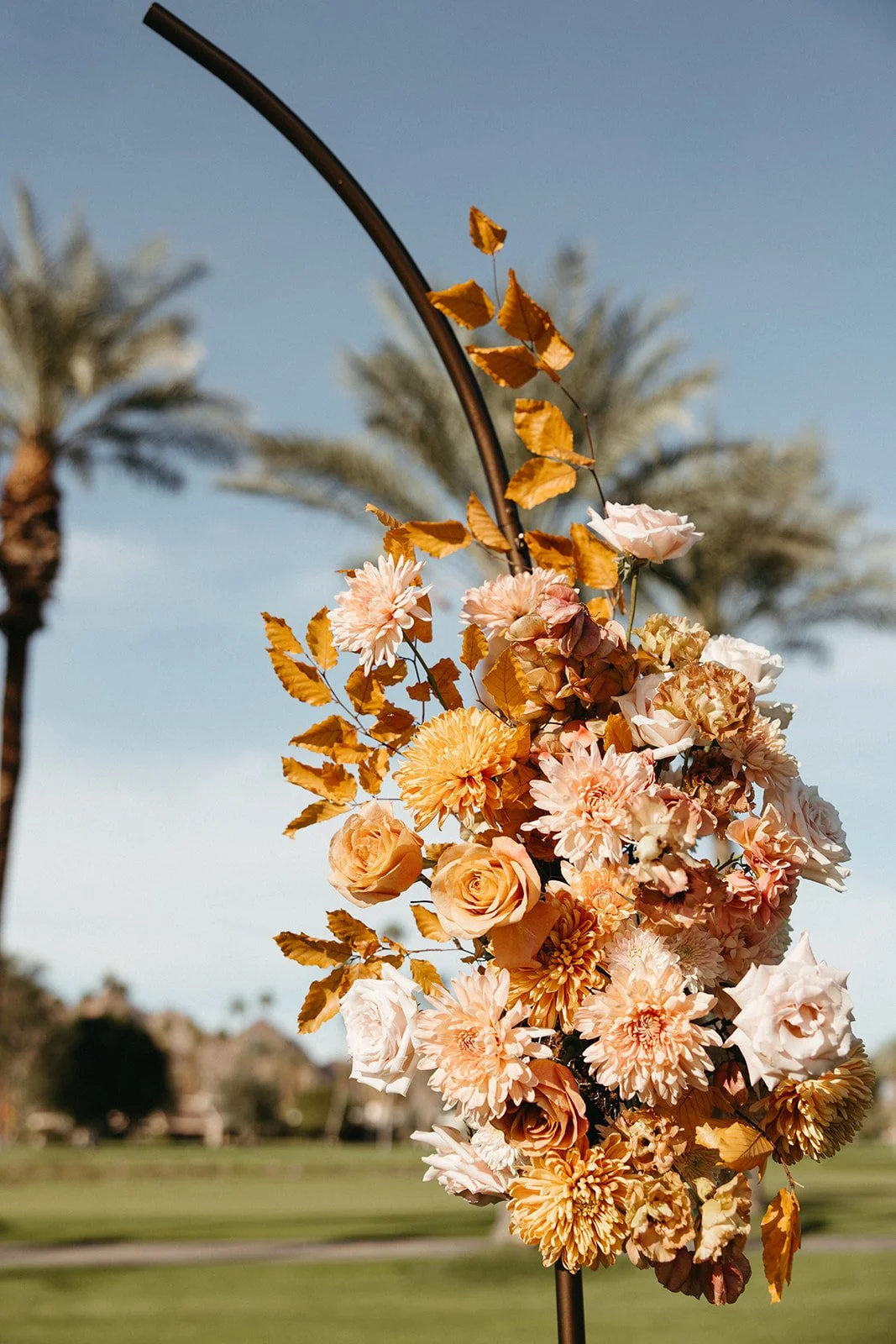 Close-up of a curved ceremony floral installation featuring peach roses, blush chrysanthemums, and autumn foliage at a La Quinta Resort wedding.