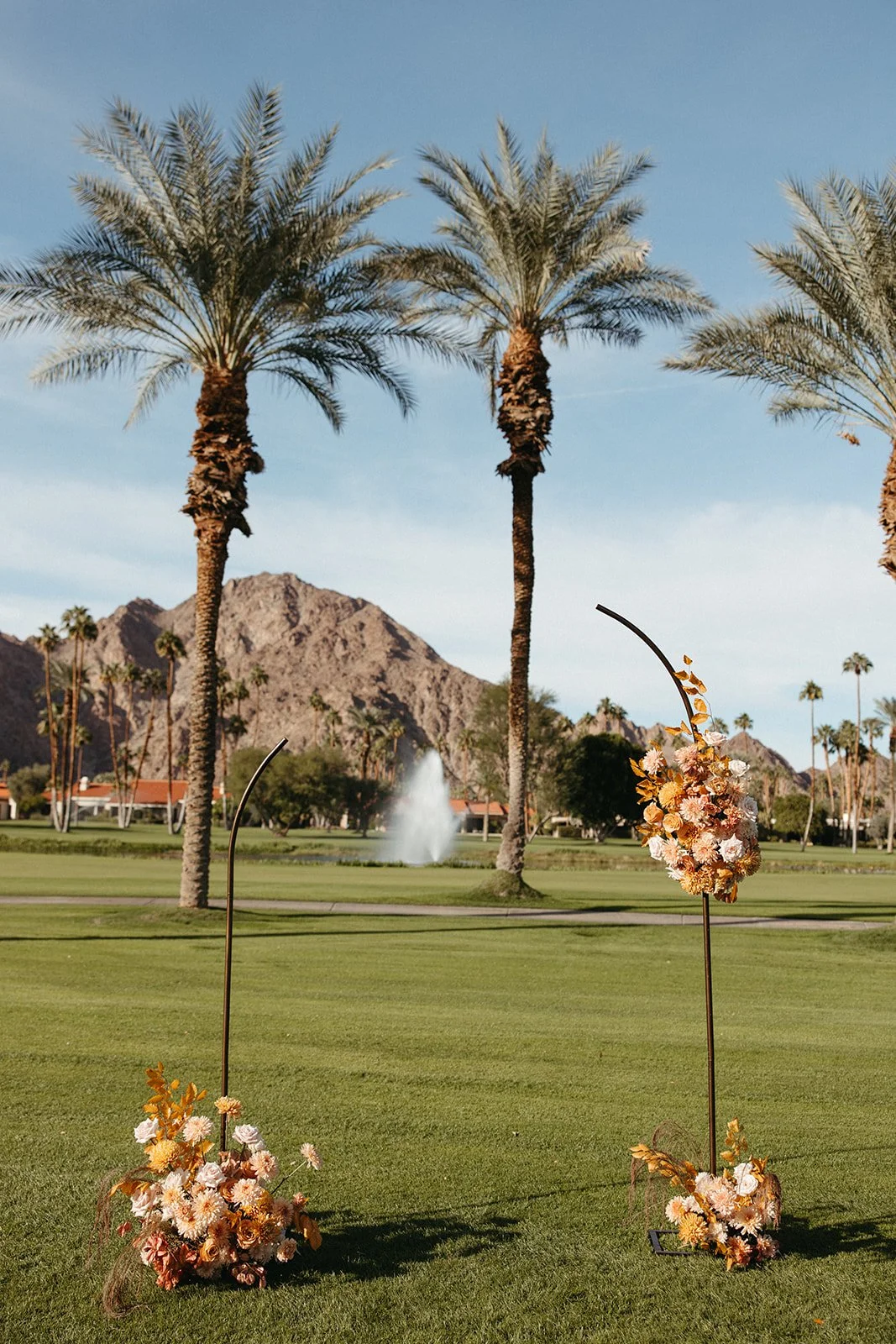 Minimalist ceremony floral installations with warm blush and golden blooms set against palm trees and mountain views at La Quinta Resort.