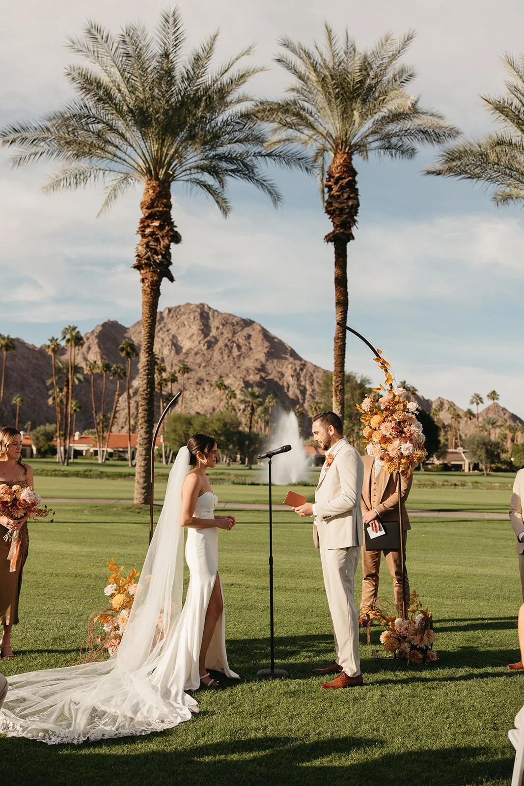 Bride and groom exchanging vows on the lawn at La Quinta Resort framed by seasonal floral installations and desert mountain view