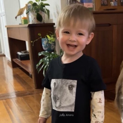 Smiling toddler wearing a black shirt with an animal print of Jaffa the Kangaroo.