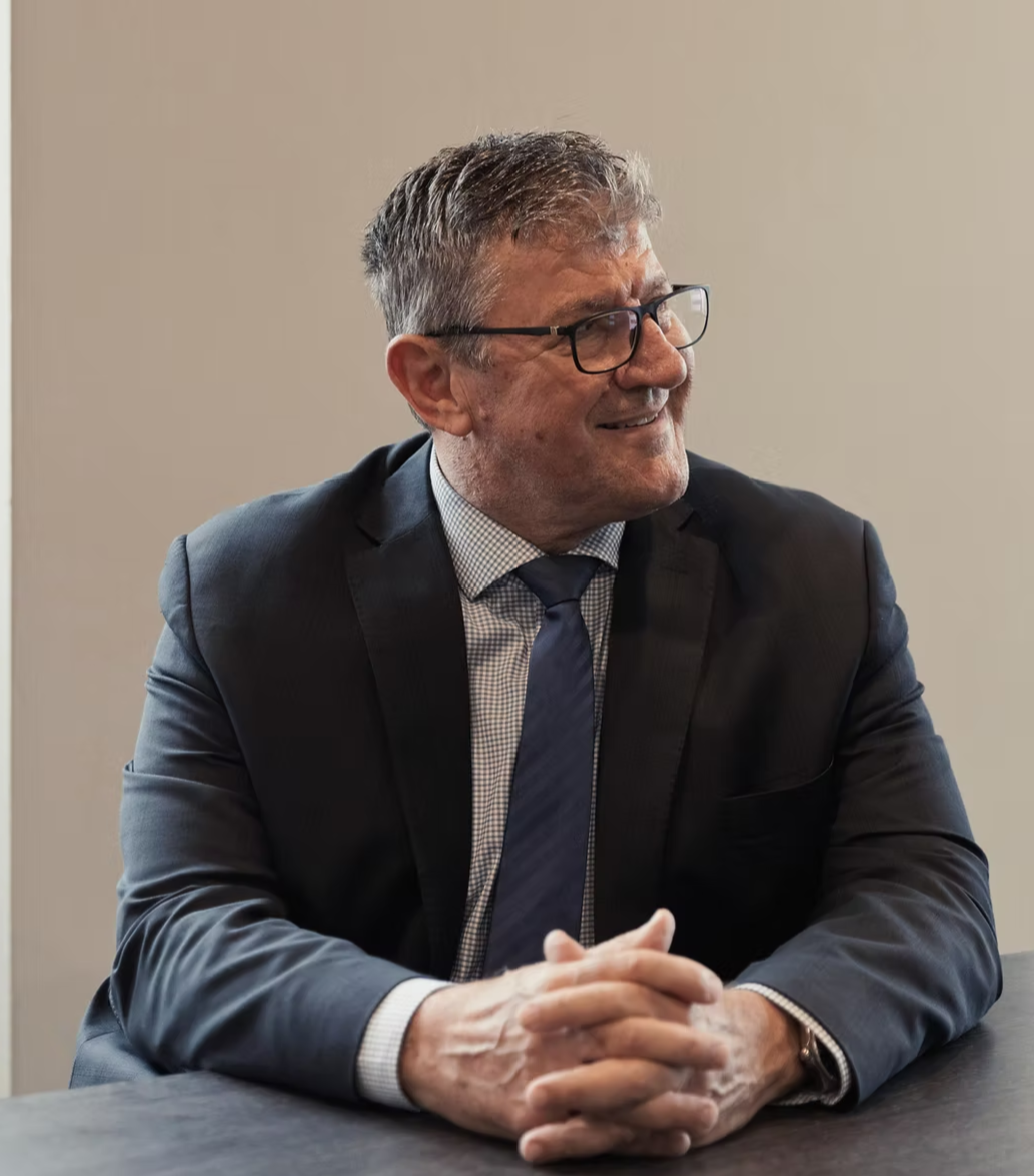 Portrait of a smiling man in a suit and tie, standing against a neutral background.