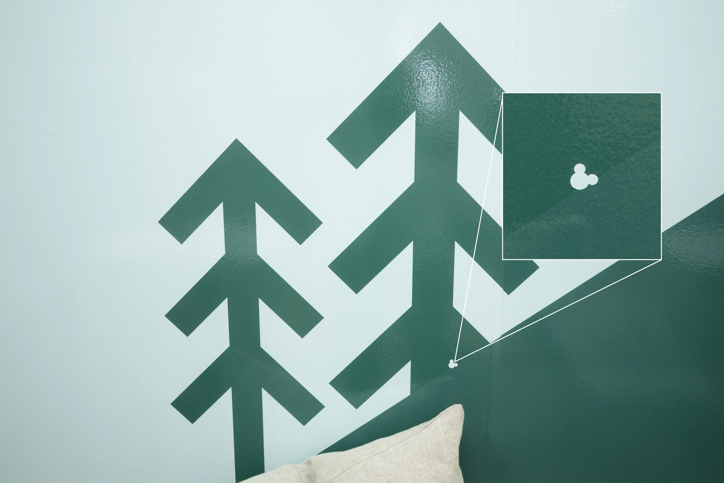 Decorative wall with multiple green arrow-shaped designs pointing upwards, and an inset illustrating a small white shape on a green background.