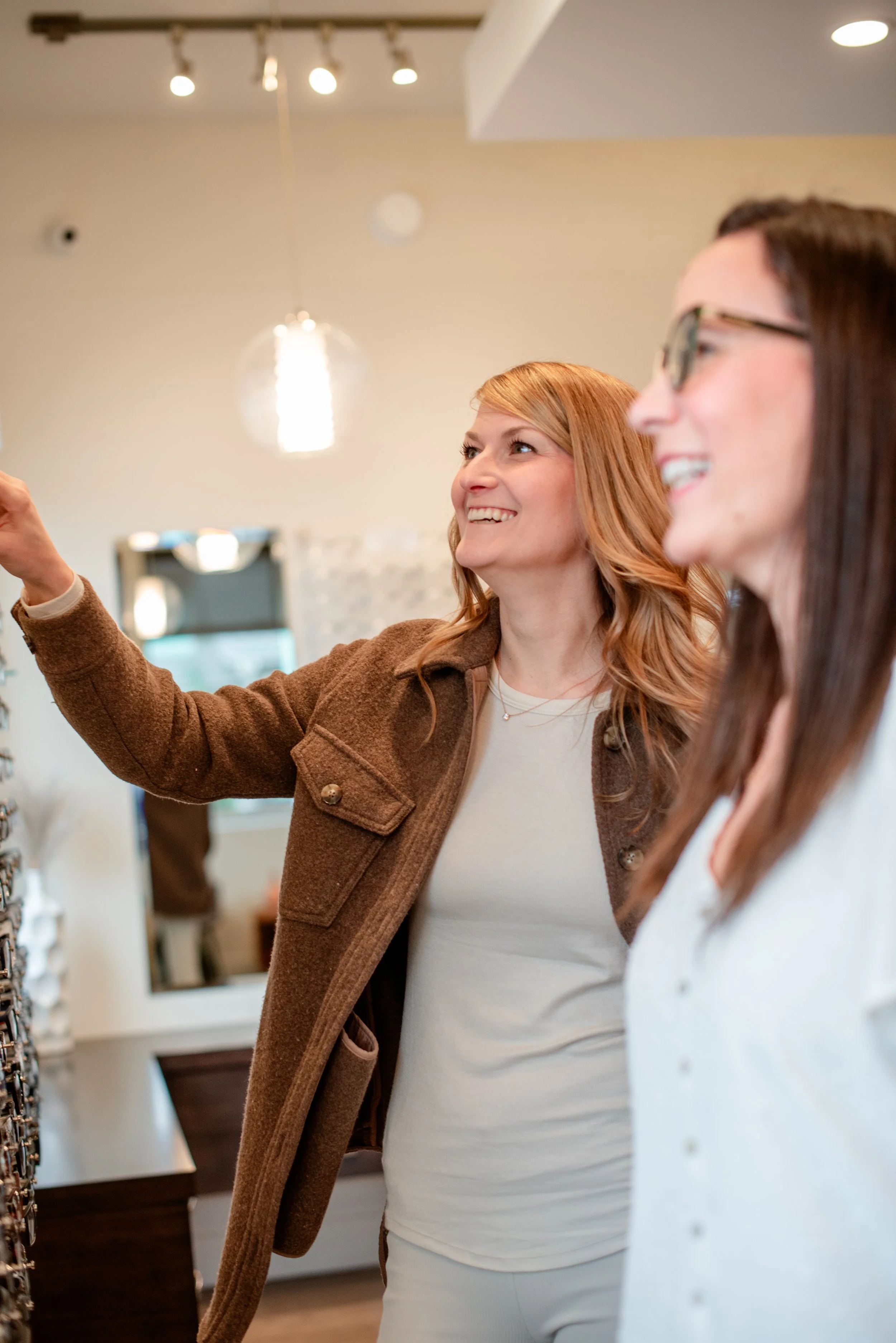 Two women smiling and shopping for glasses in a store.