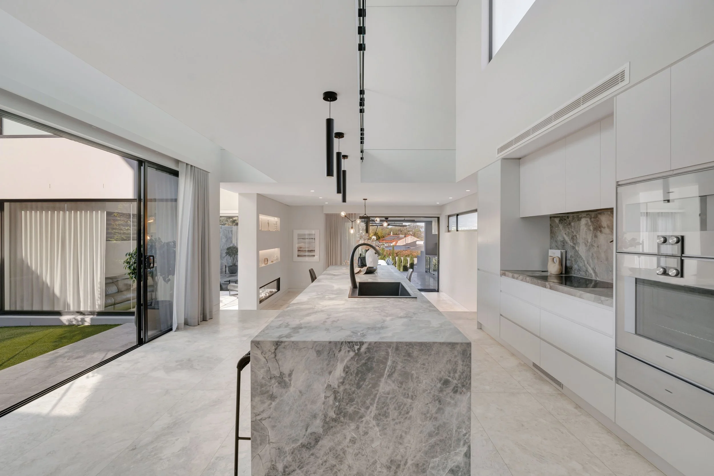 Modern kitchen with white cabinets, marble island, black pendant lights, and large sliding glass doors to outdoor area