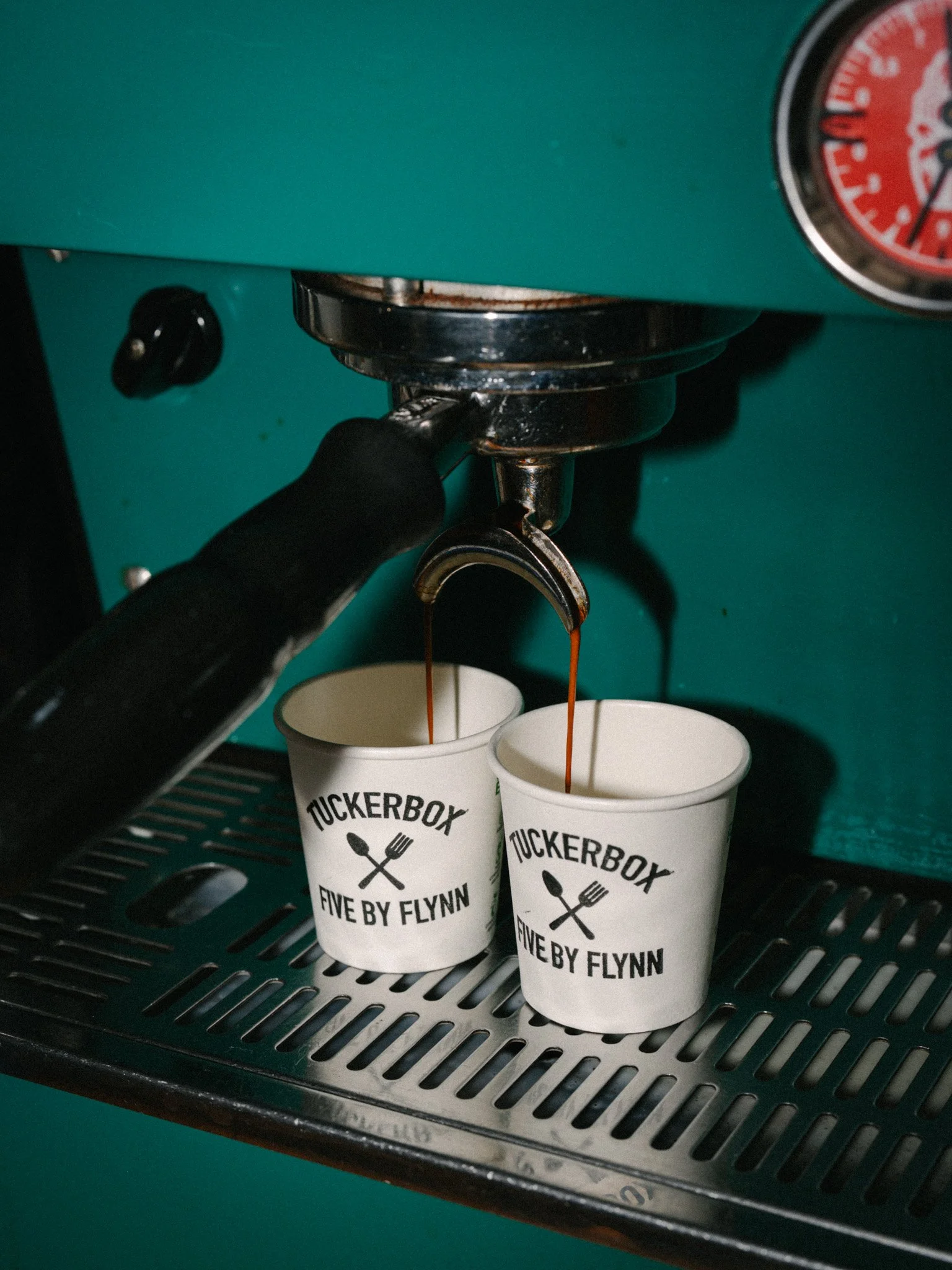 Two cups being filled with coffee from an espresso machine labeled 'TUCKERBOX FIVE BY FLYNN'.