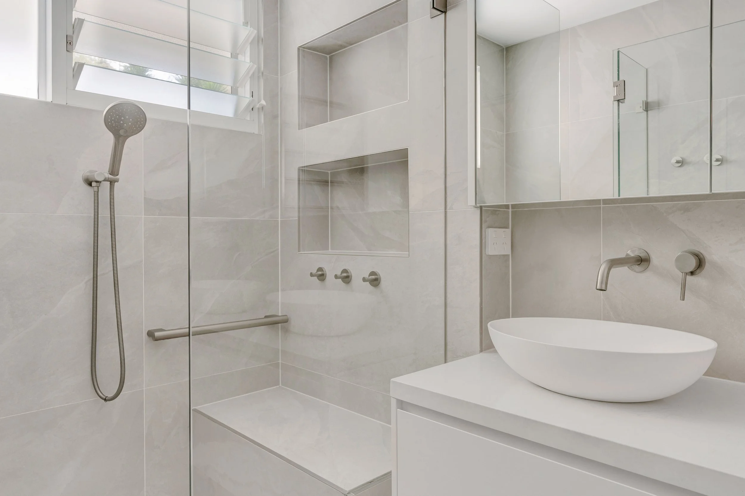Modern bathroom with a walk-in shower, built-in shelves, a white sink, and a mirror.