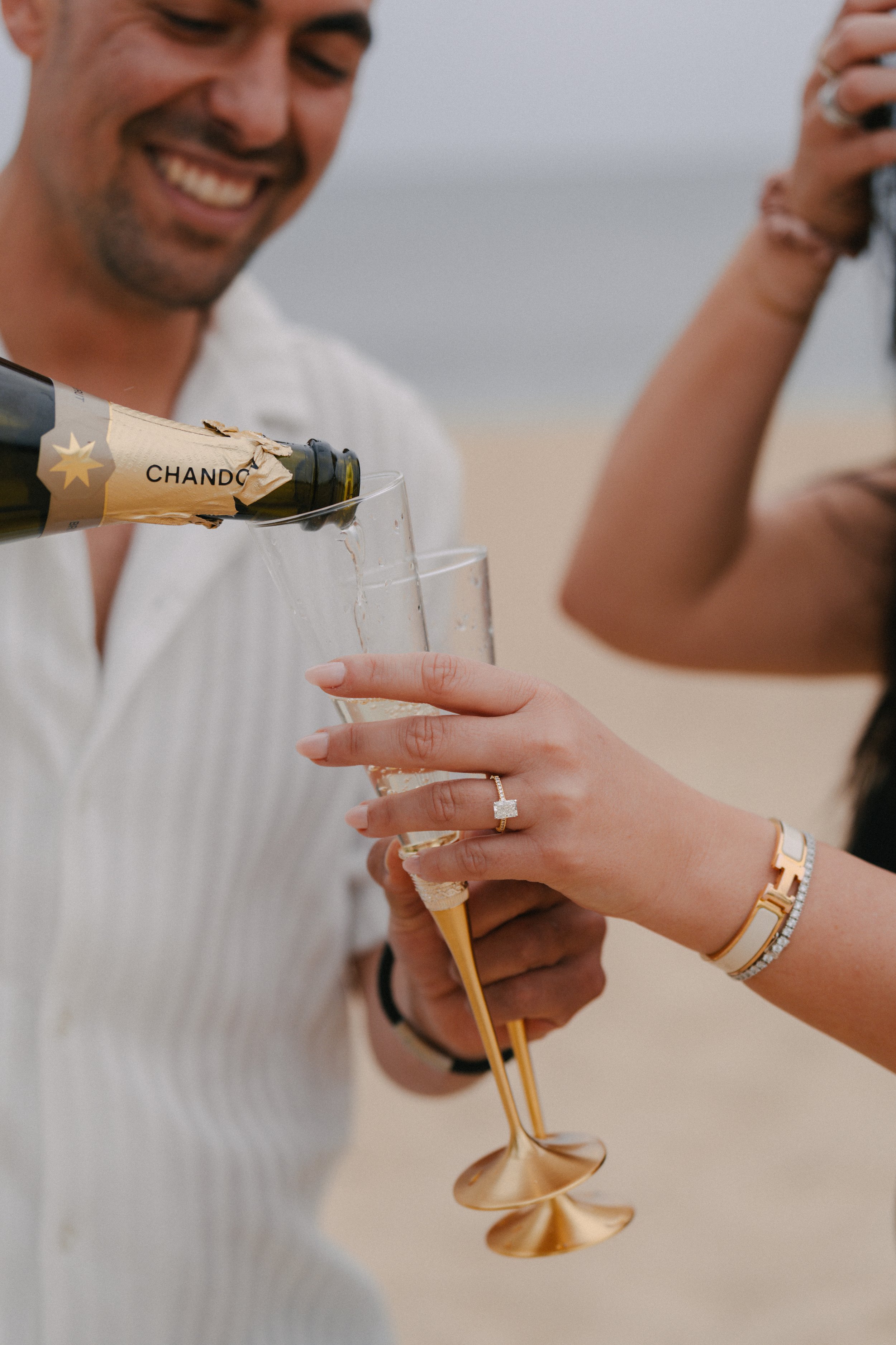 People on the beach celebrating with champagne, pouring drinks into glasses with the sea in the background.