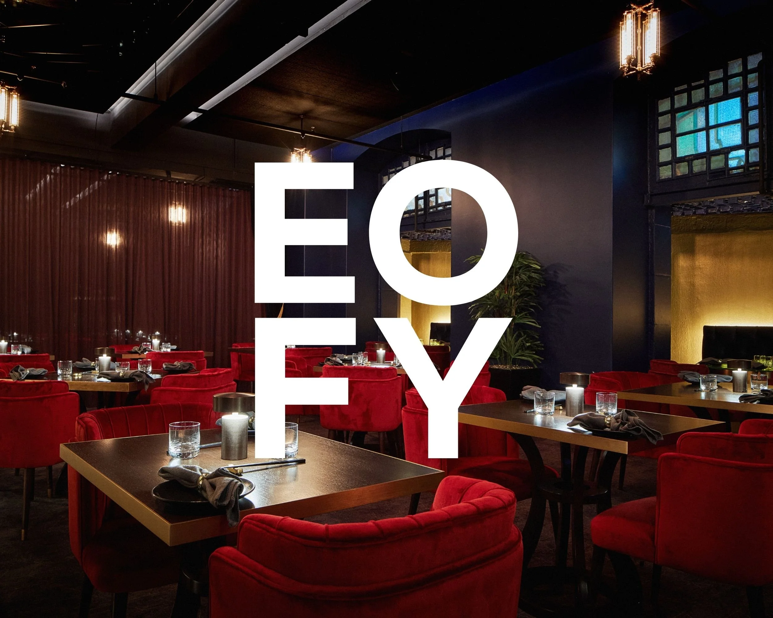 A stylish restaurant interior with red velvet chairs, dark wood tables set with glasses and cloth napkins, warm lighting, dark walls, and decorative lighting fixtures, creating an elegant atmosphere.