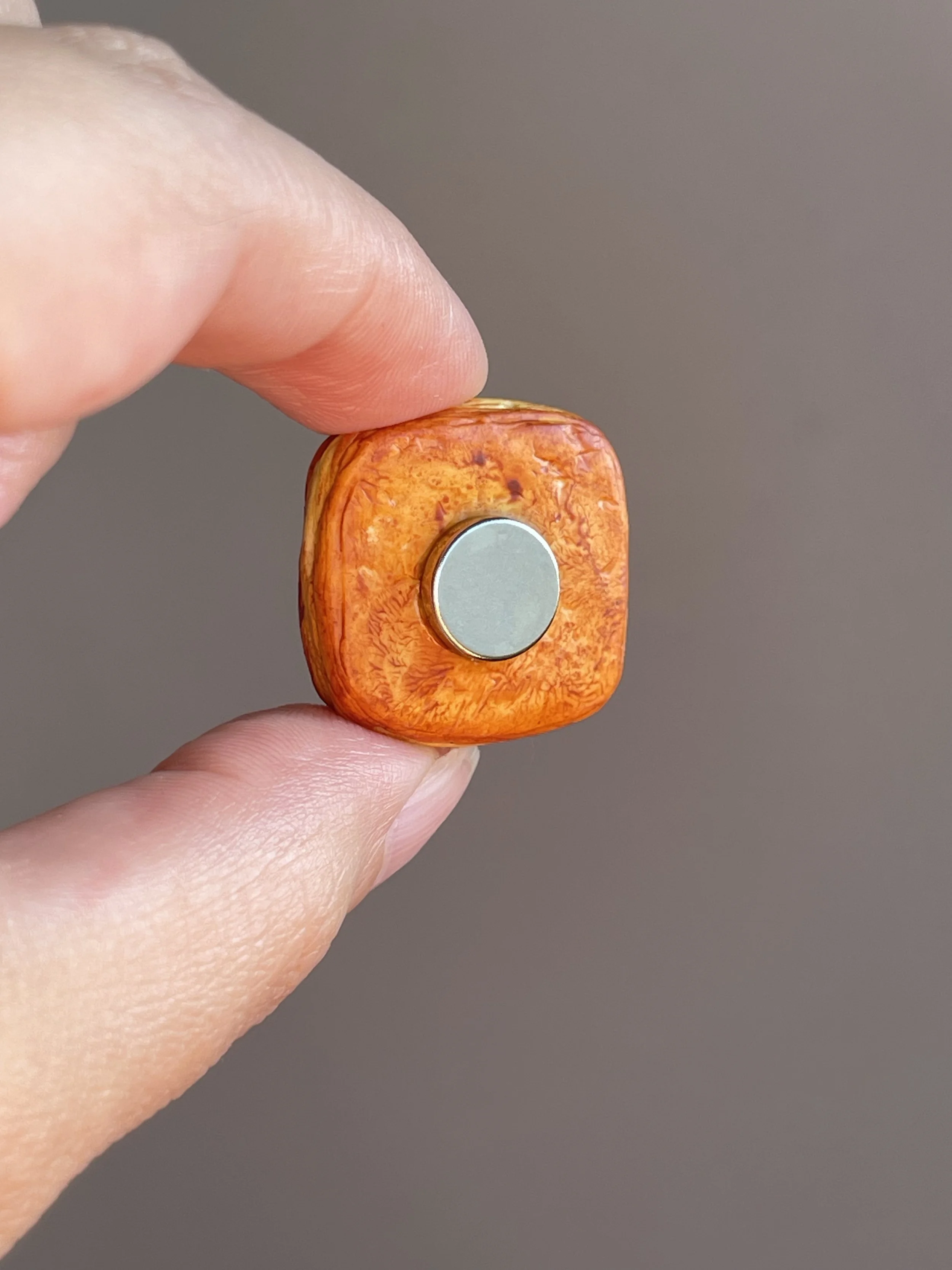 Fingers holding a miniature polymer clay danish with custard and strawberry slices magnet showing the back.