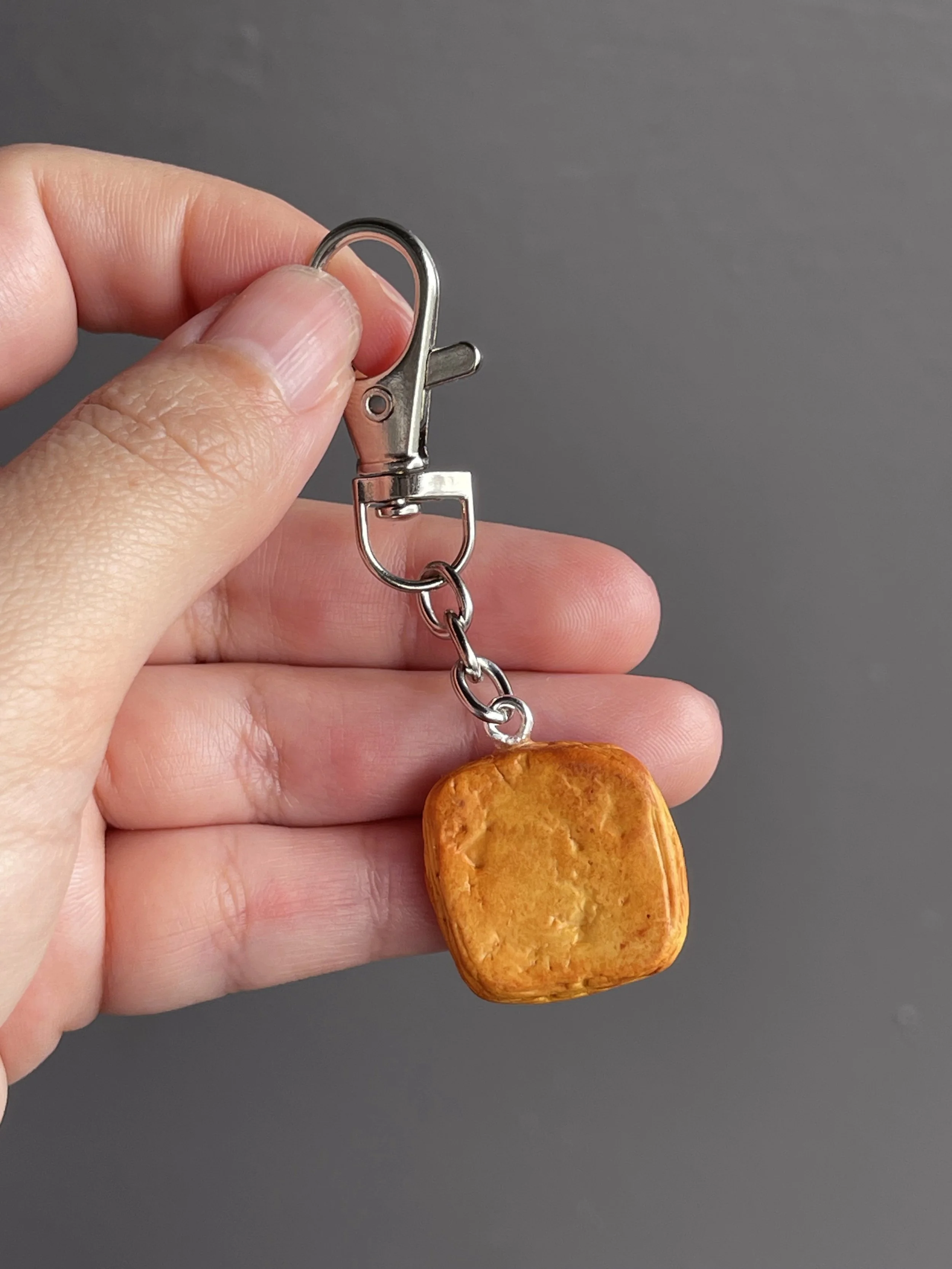 A hand holding a miniature polymer clay egg danish keychain with runny egg yolk showing the back of the piece.
