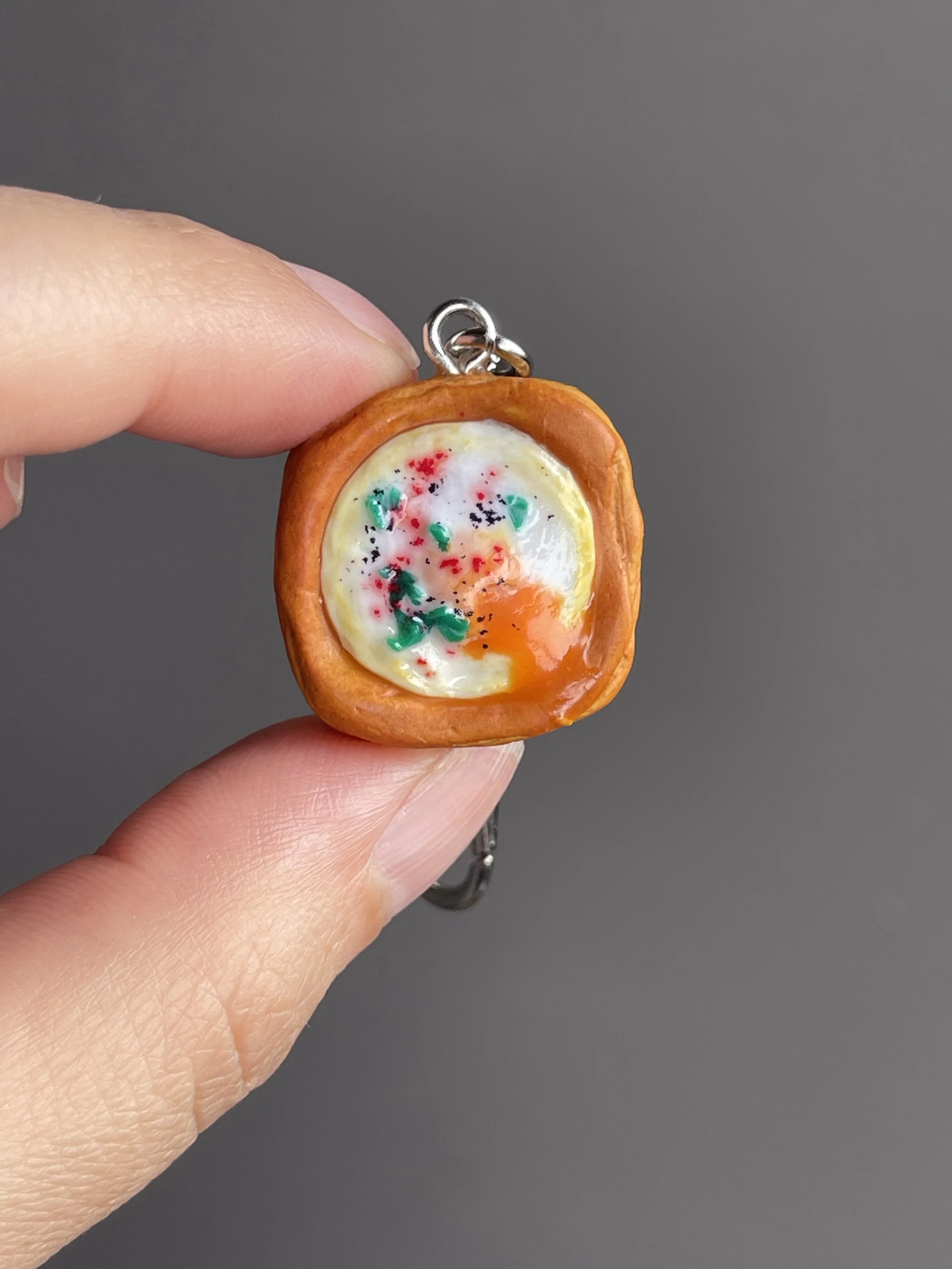 A hand holding a miniature polymer clay egg danish keychain with runny egg yolk.