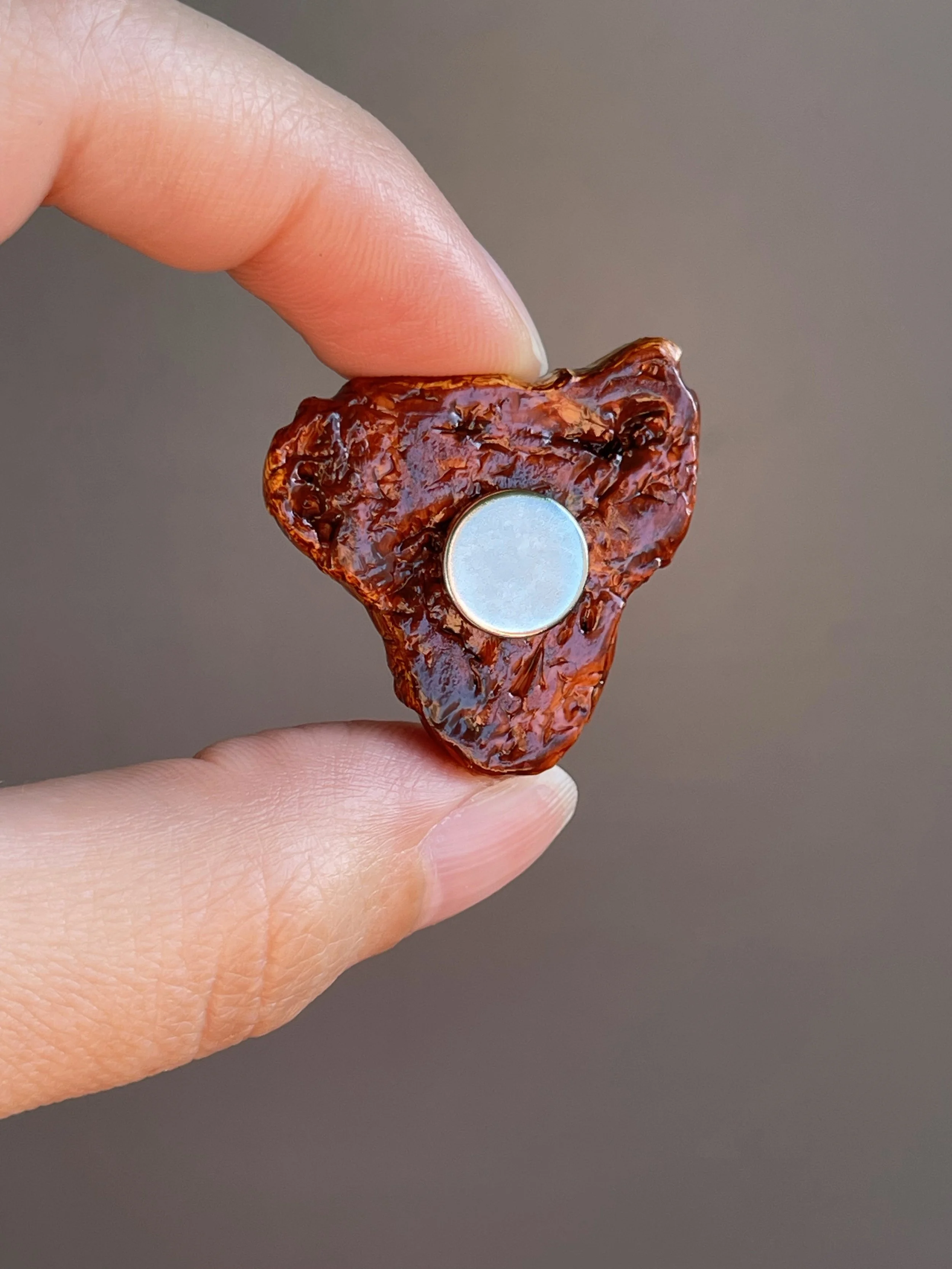 Fingers holding a realistic polymer clay t-bone steak magnet showing the back.
