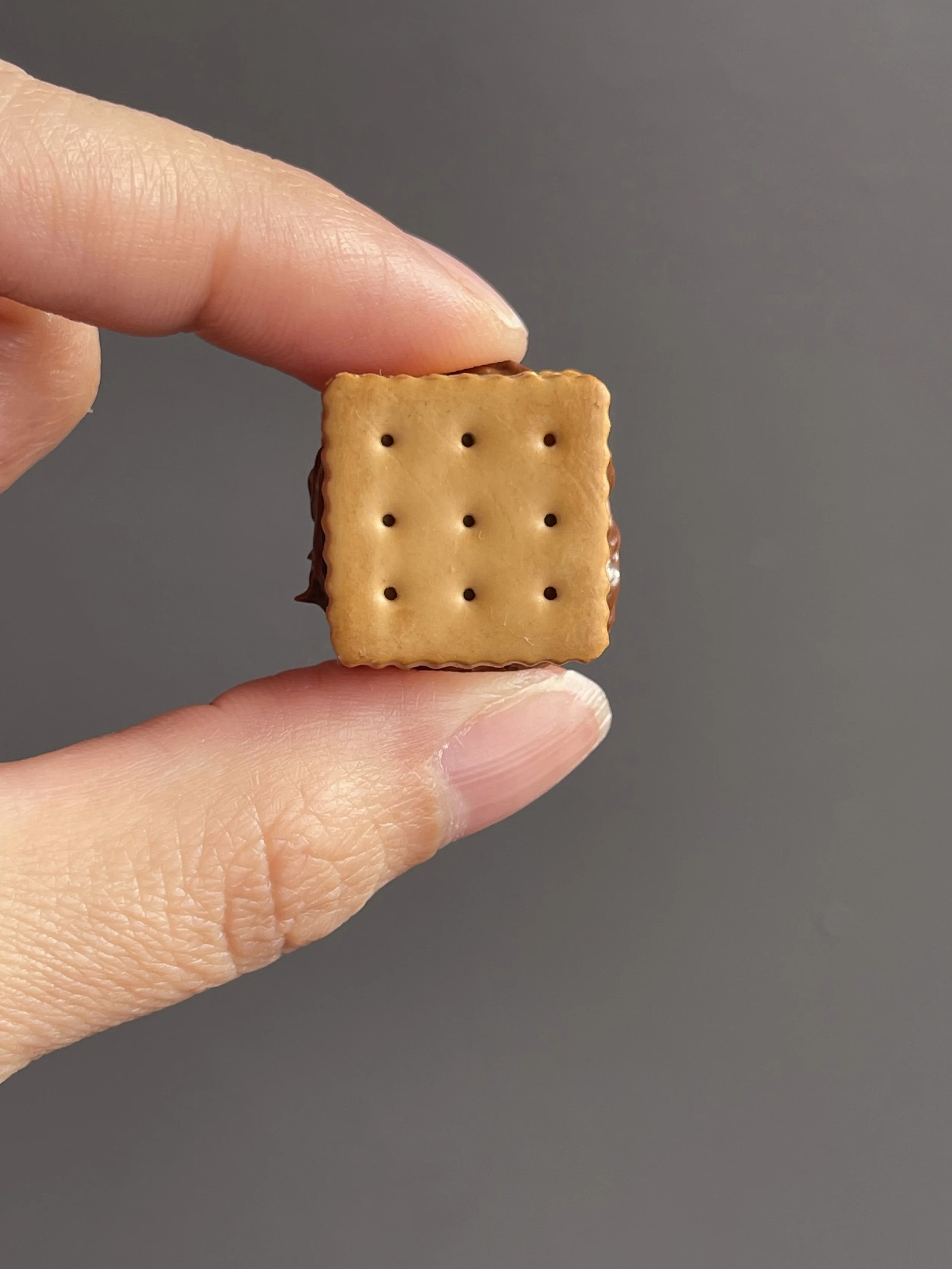 Fingers holding a miniature polymer clay s’more magnet.