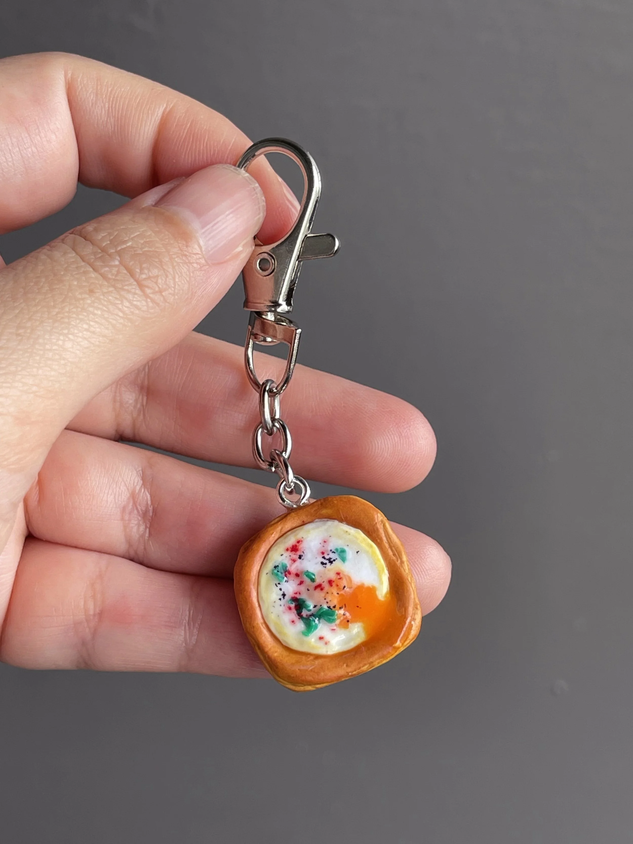 A hand holding a miniature polymer clay egg danish keychain with runny egg yolk.