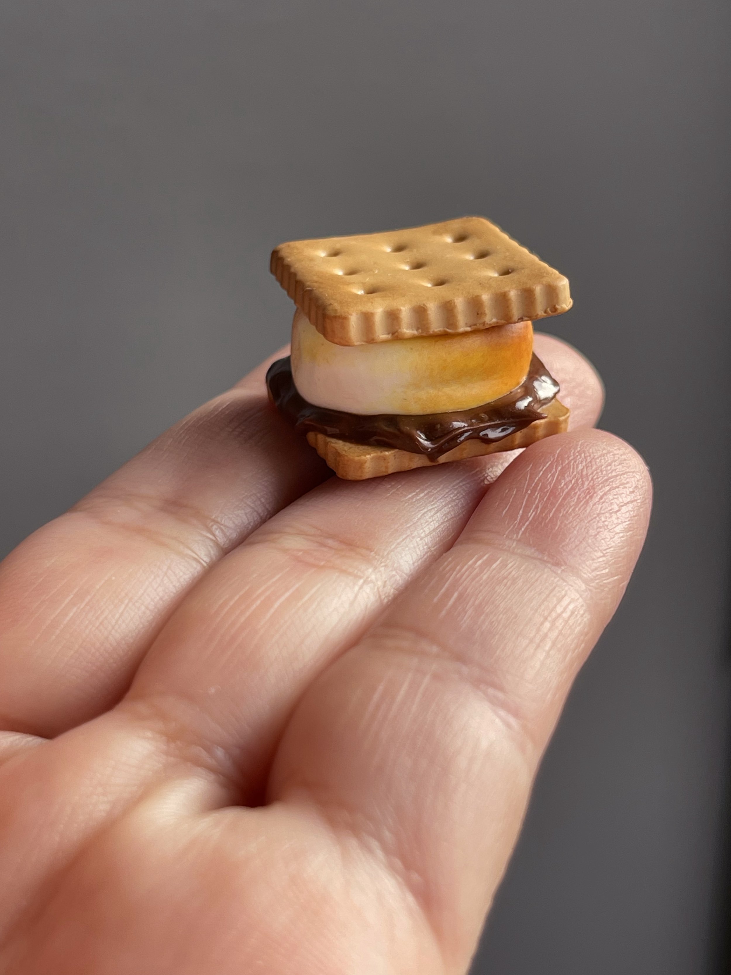 A hand holding a miniature polymer clay s’more magnet.