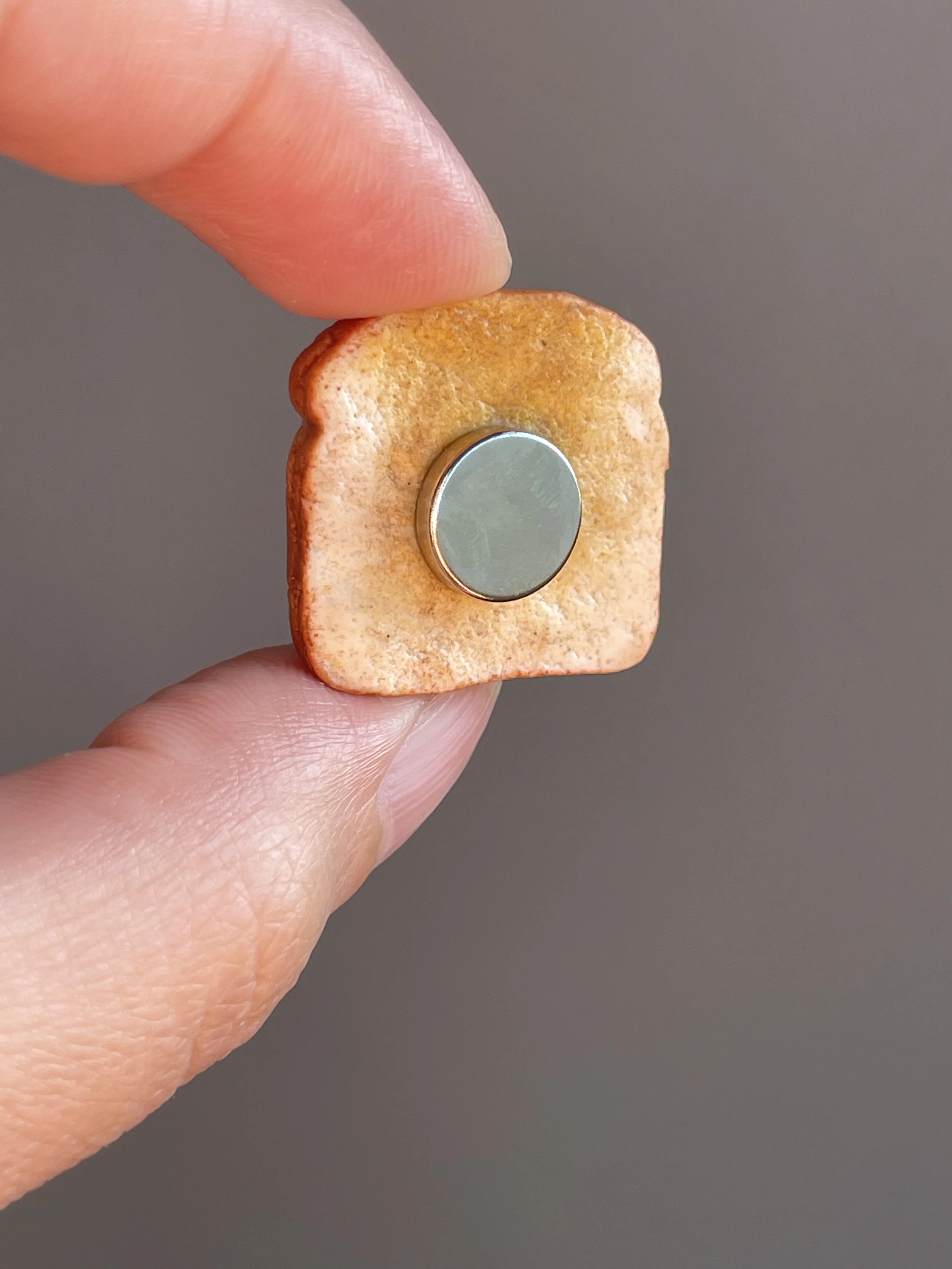 Fingers holding a miniature polymer clay hazelnut spread and figs toast magnet showing the back.