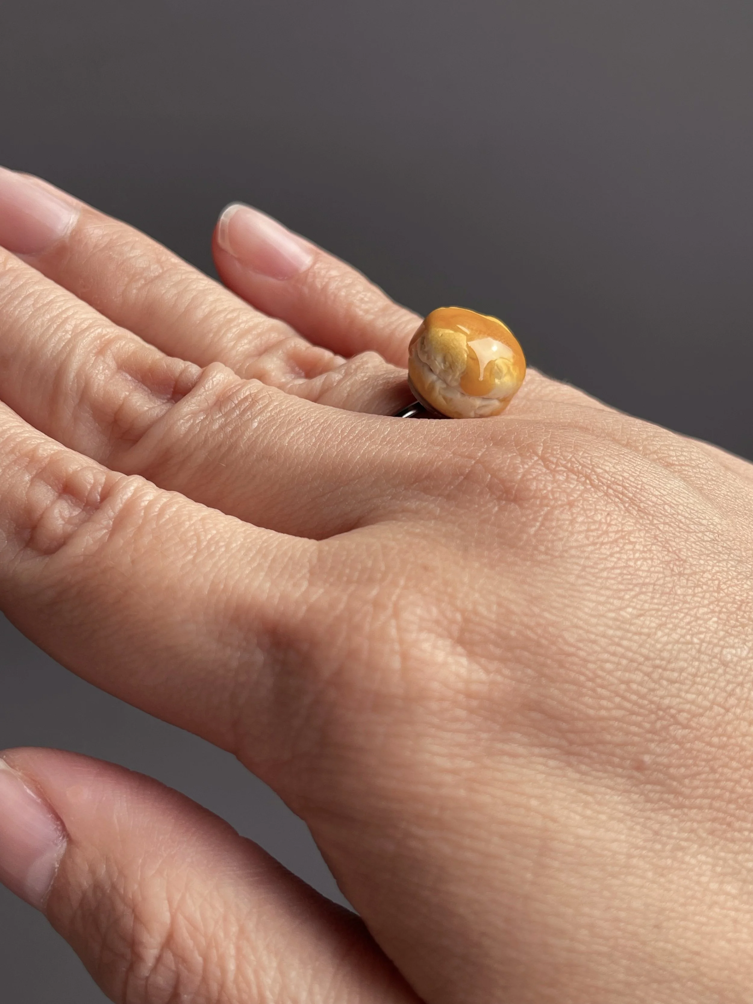 A hand wearing an adjustable ring topped with a miniature polymer clay biscuit with resin dripping honey.