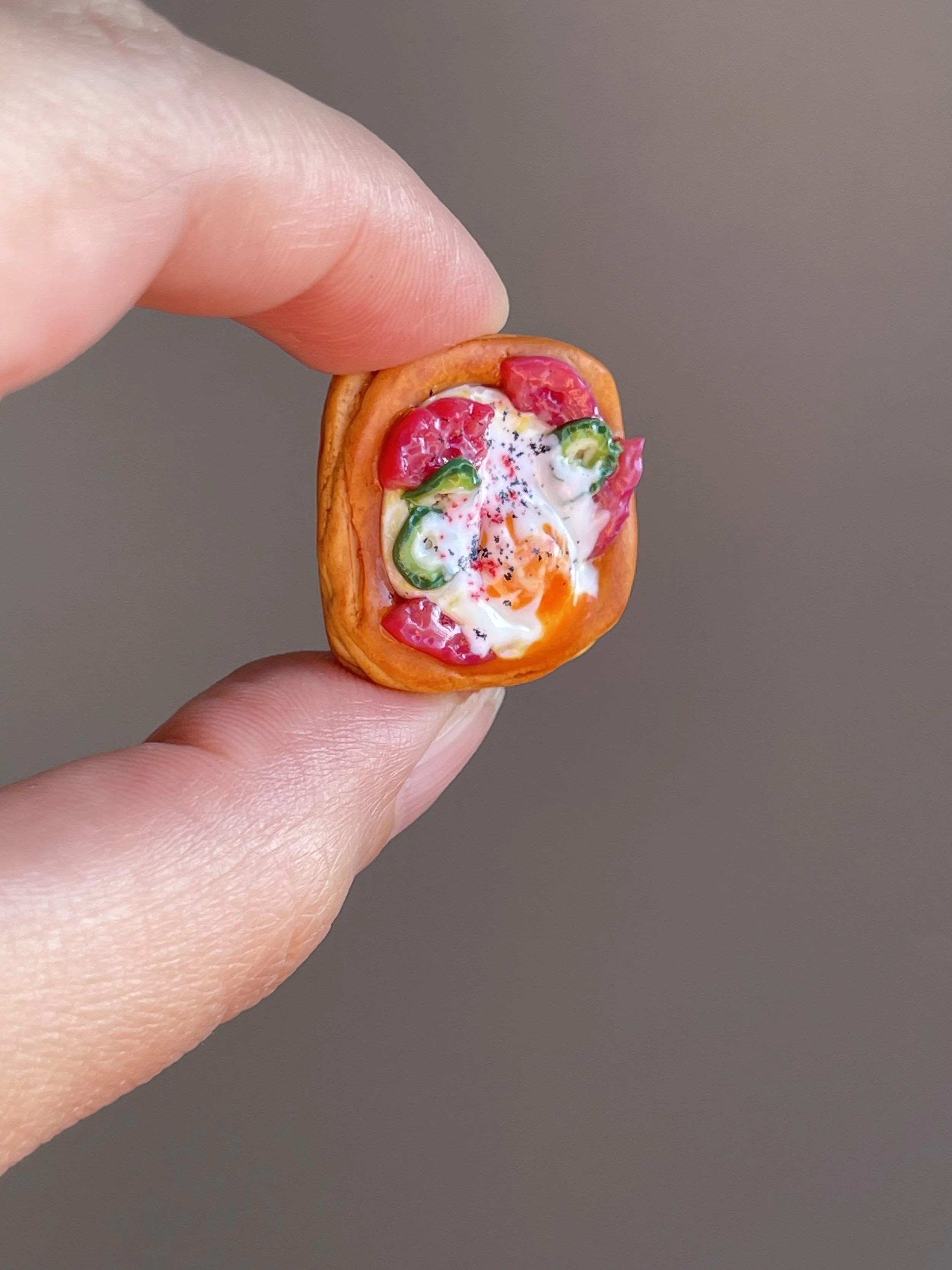 Fingers holding a miniature polymer clay egg, tomato, jalapeño breakfast danish magnet.