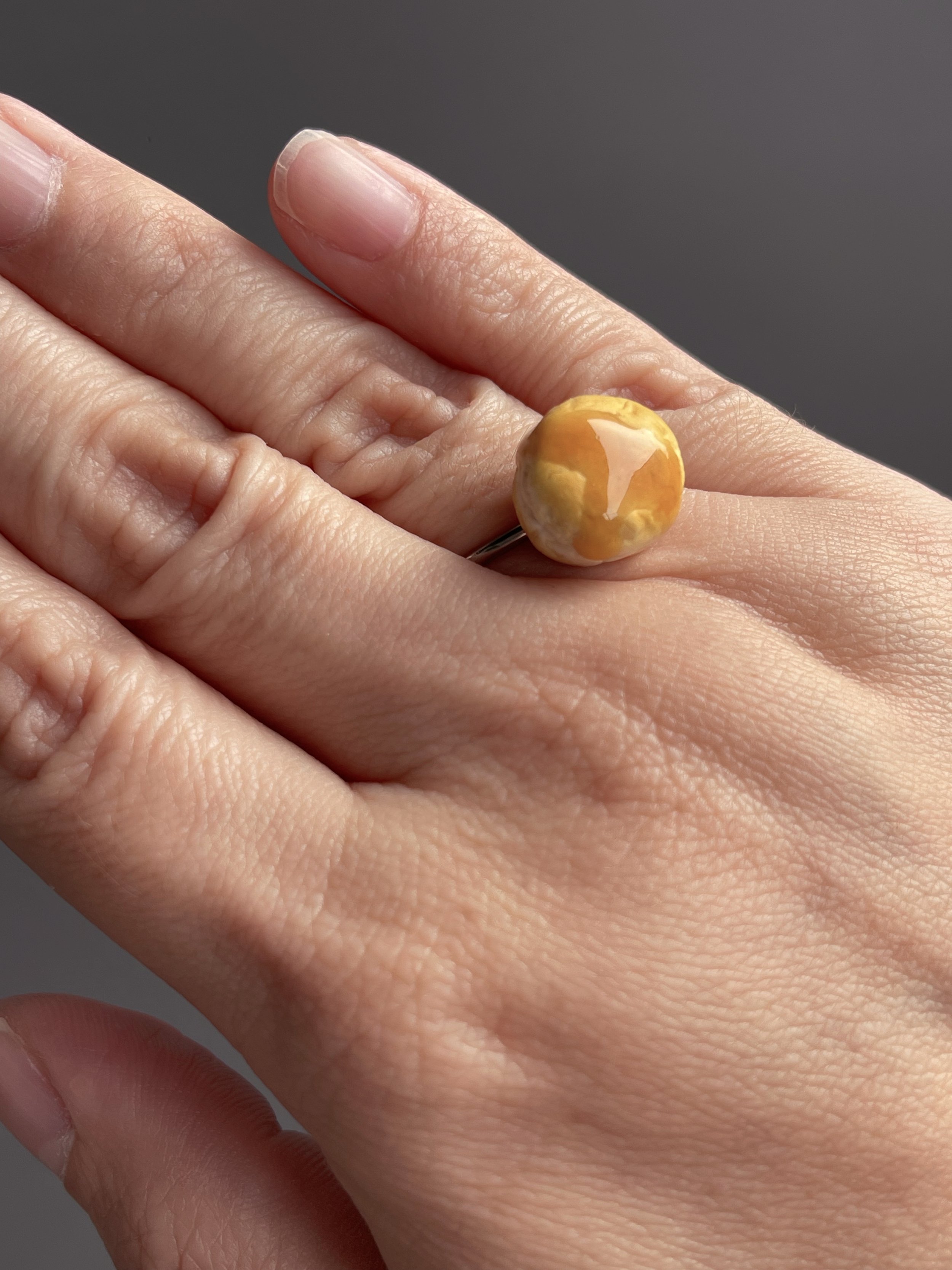 A hand wearing an adjustable ring topped with a miniature polymer clay biscuit with resin dripping honey.