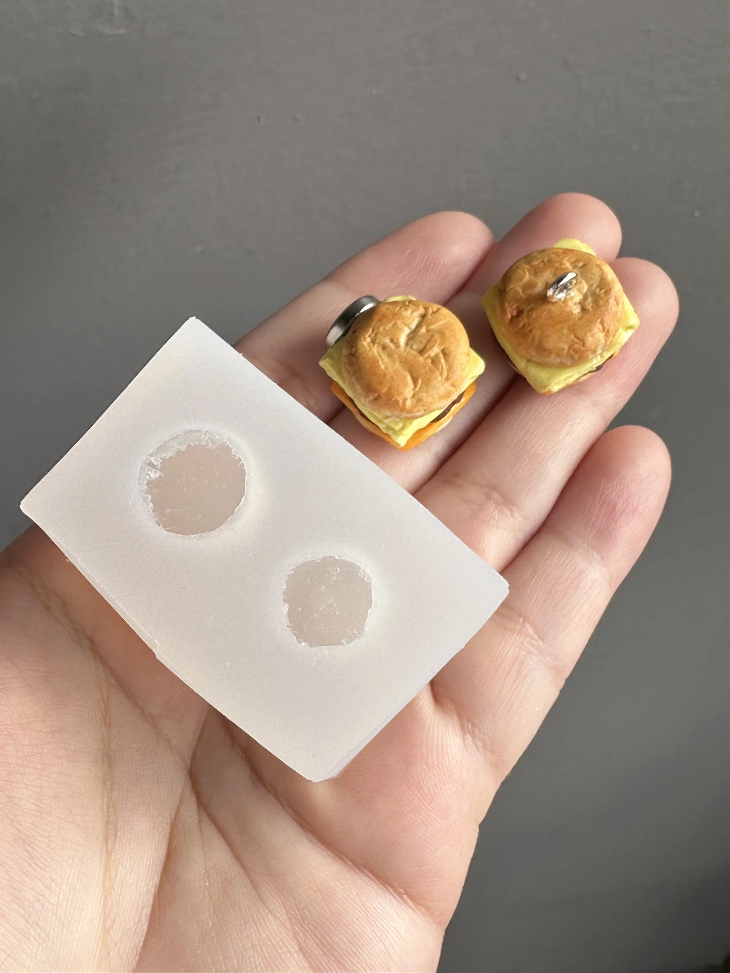 A hand holding a mini biscuits duo silicone mold with samples of the types of biscuits that can be made from the mold.