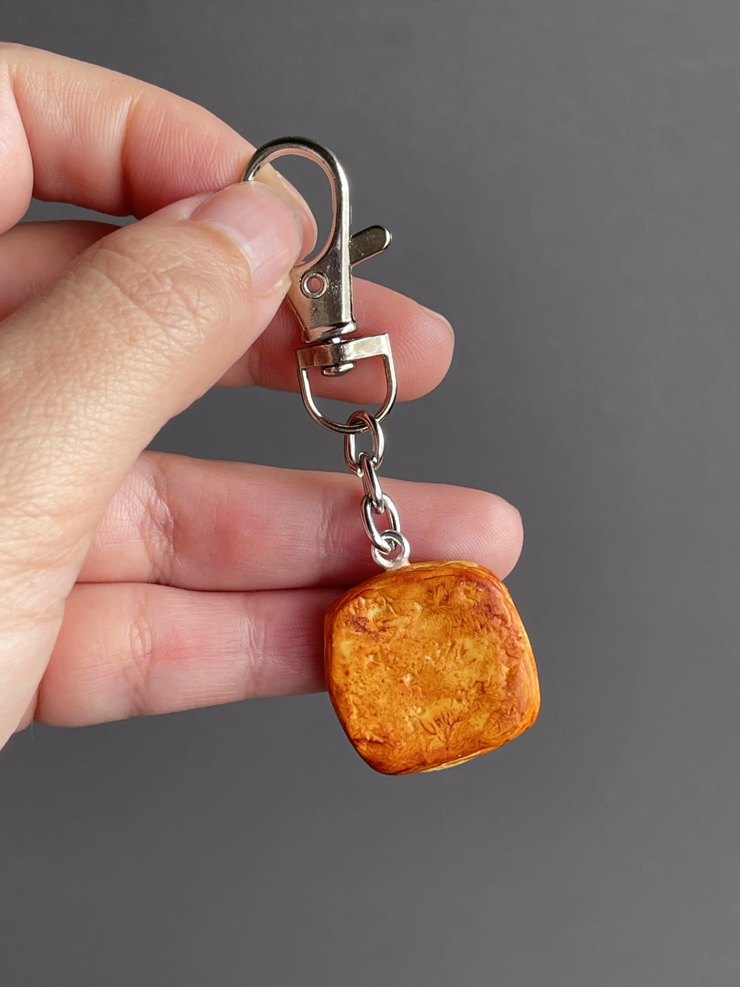 A hand holding a miniature danish pastry with yellow custard and strawberry slices keychain showing the back of the piece.