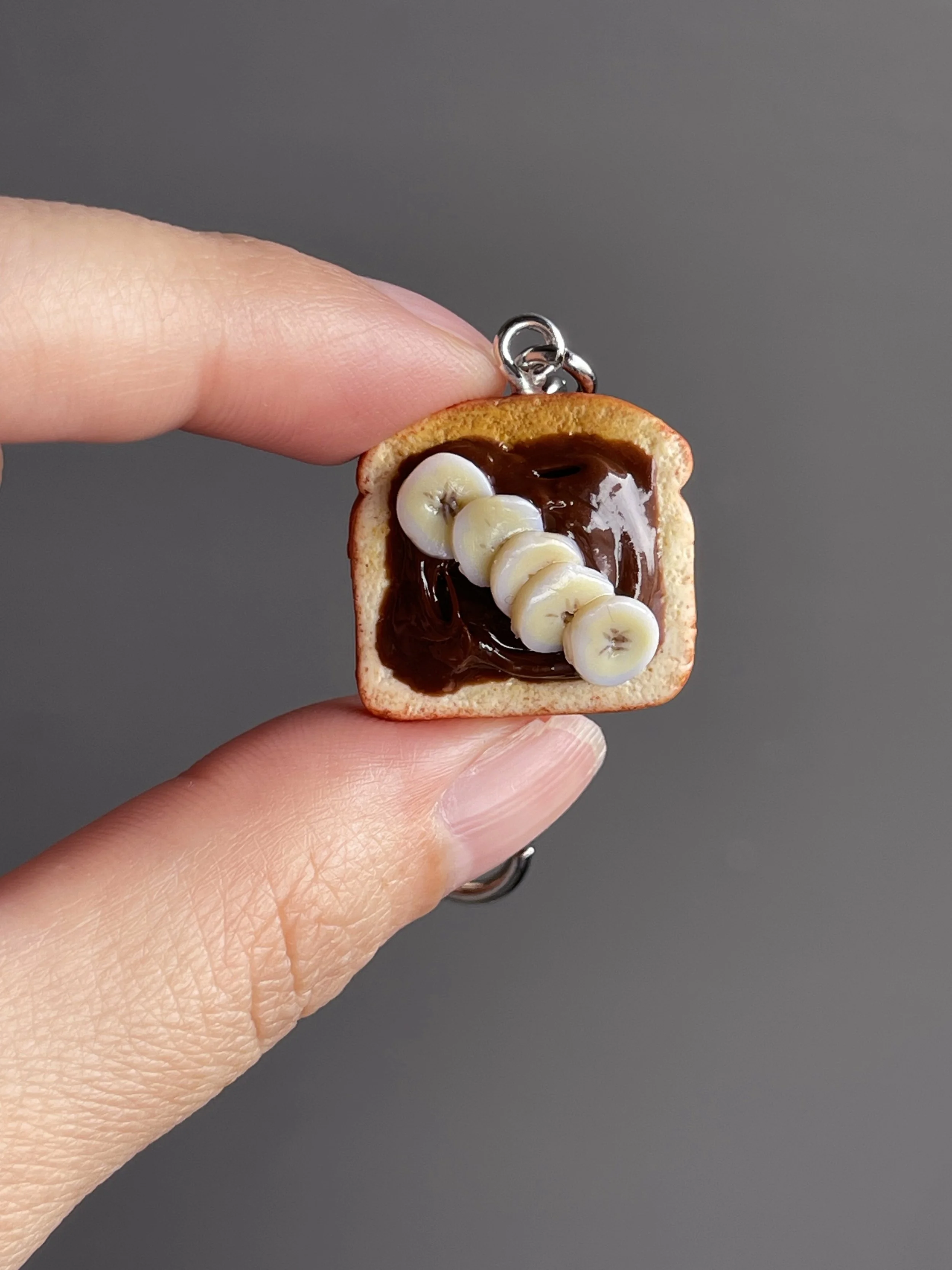 A hand holding a miniature polymer clay toast with hazelnut spread and banana slices.