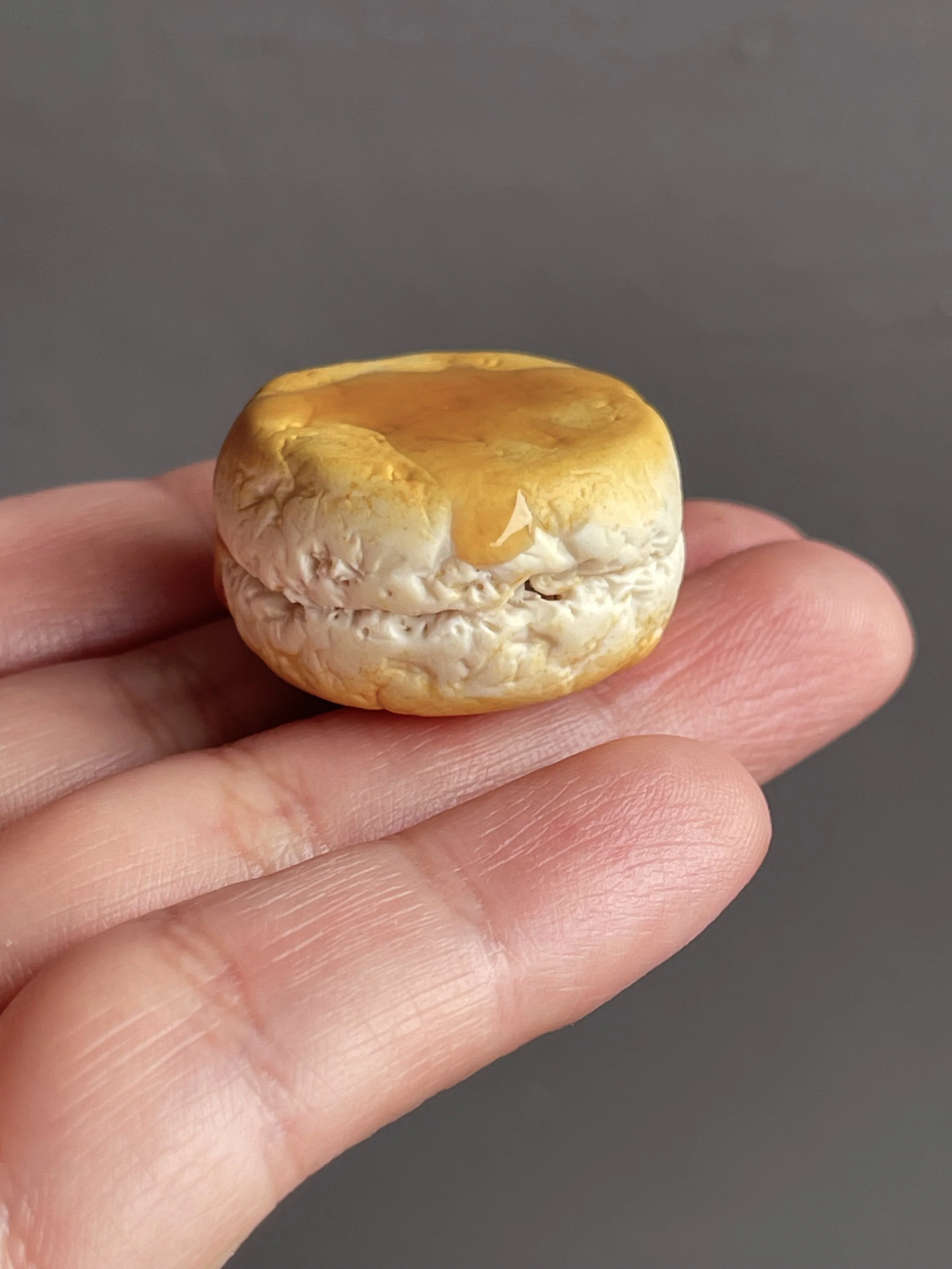 A hand holding a polymer clay biscuit and honey magnet.