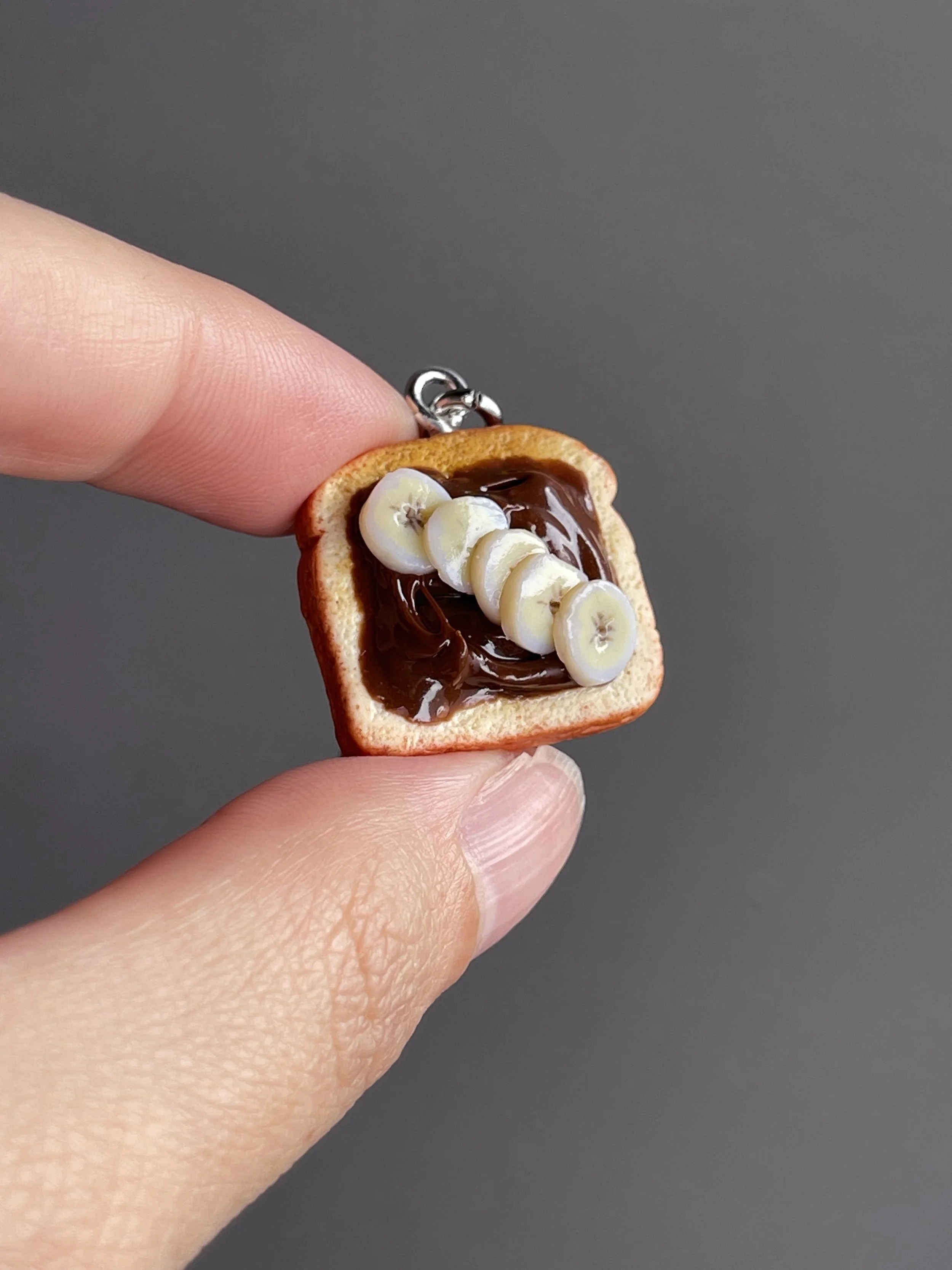 A hand holding a miniature polymer clay toast with hazelnut spread and banana slices.
