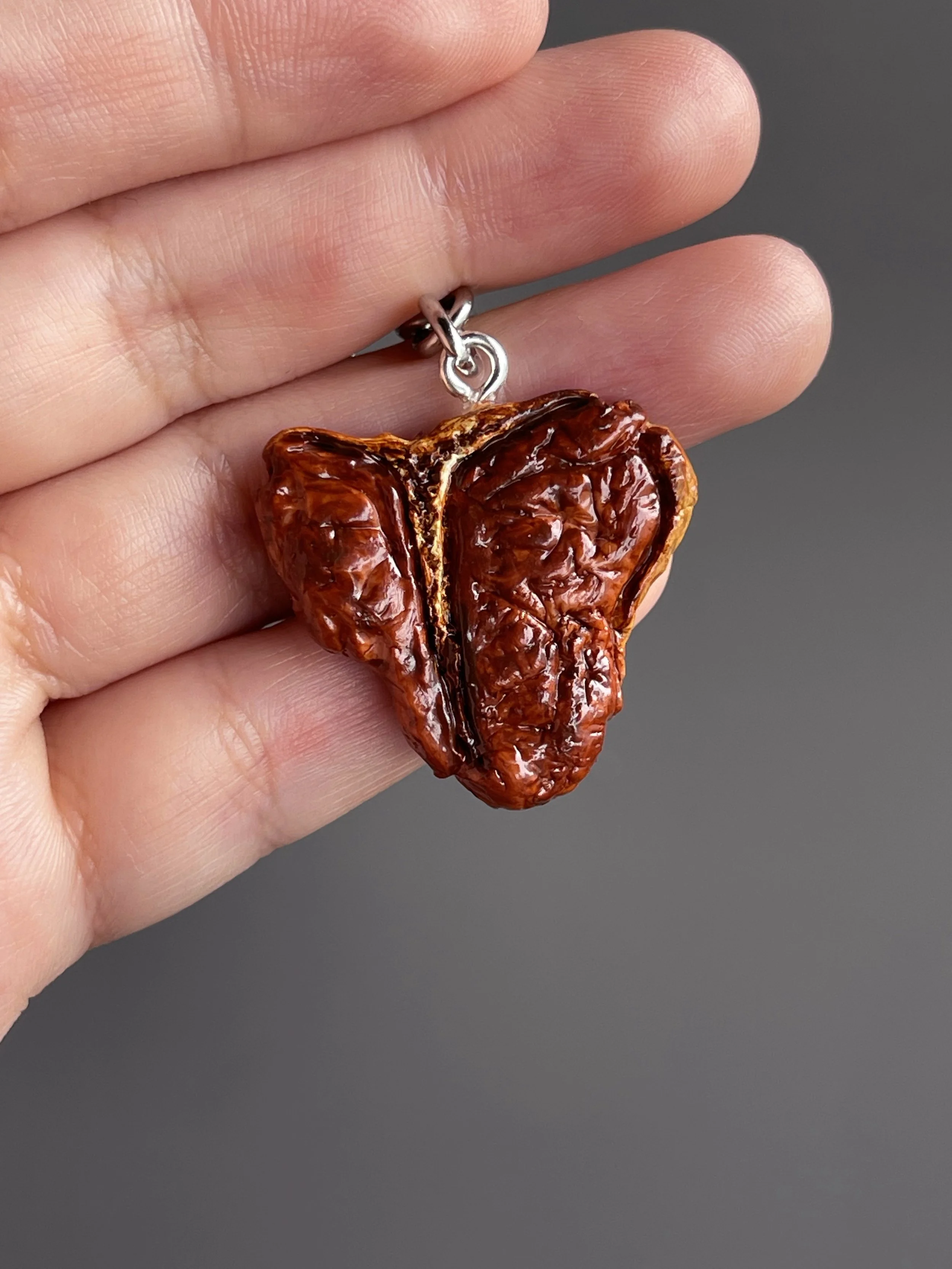 A hand holding a realistic miniature polymer clay t-bone steak keychain.