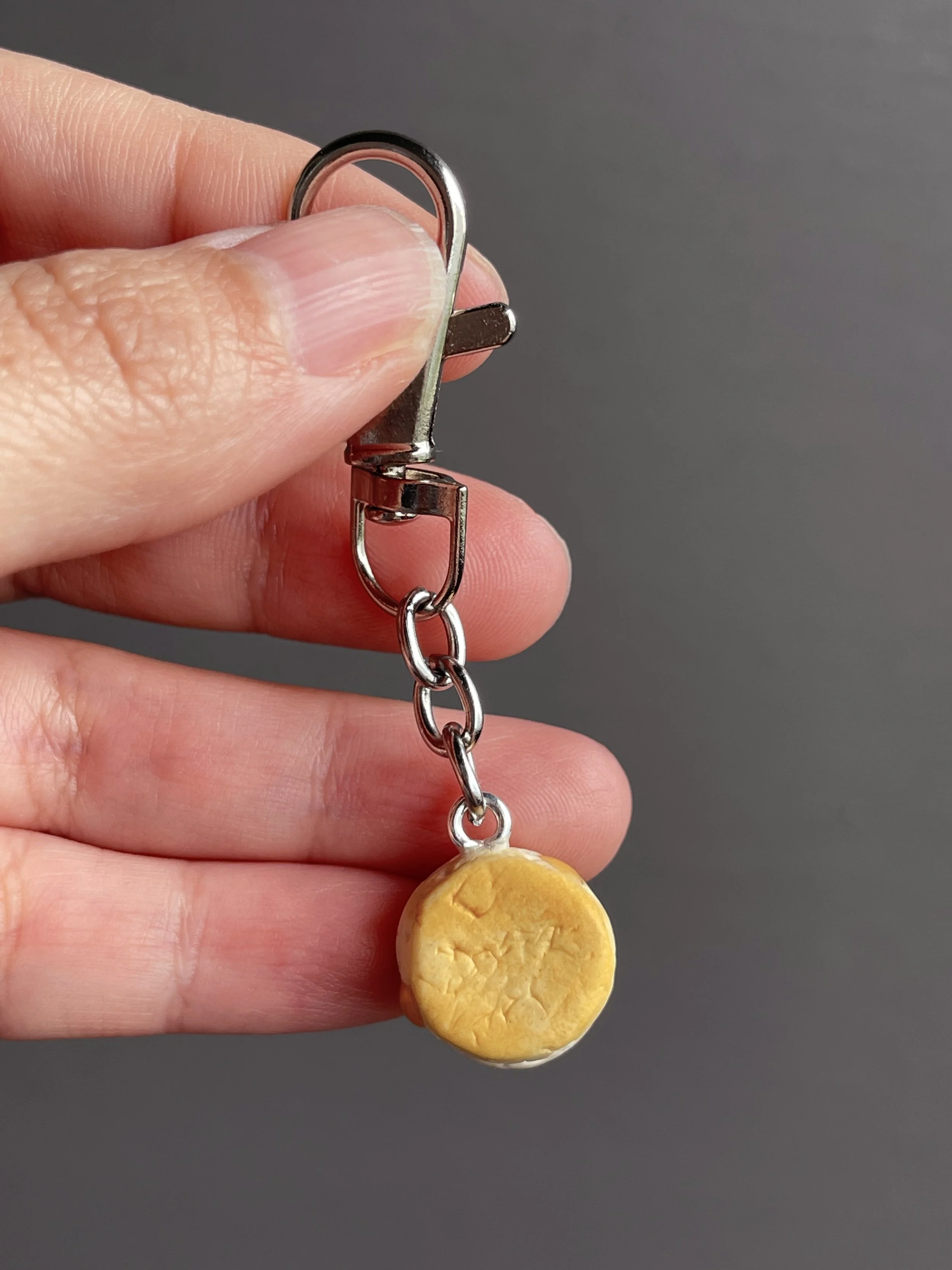 A hand holding a mini polymer clay biscuit and honey keychain showing the back.