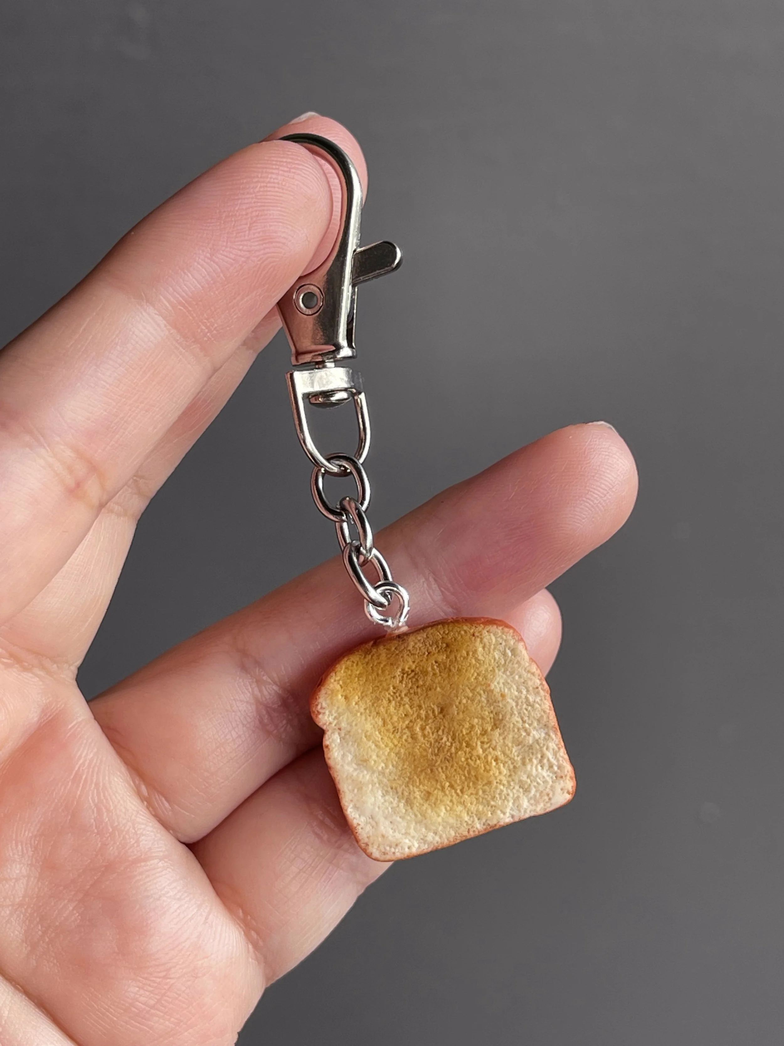 A hand holding a miniature polymer clay keychain showing the back of the toast.
