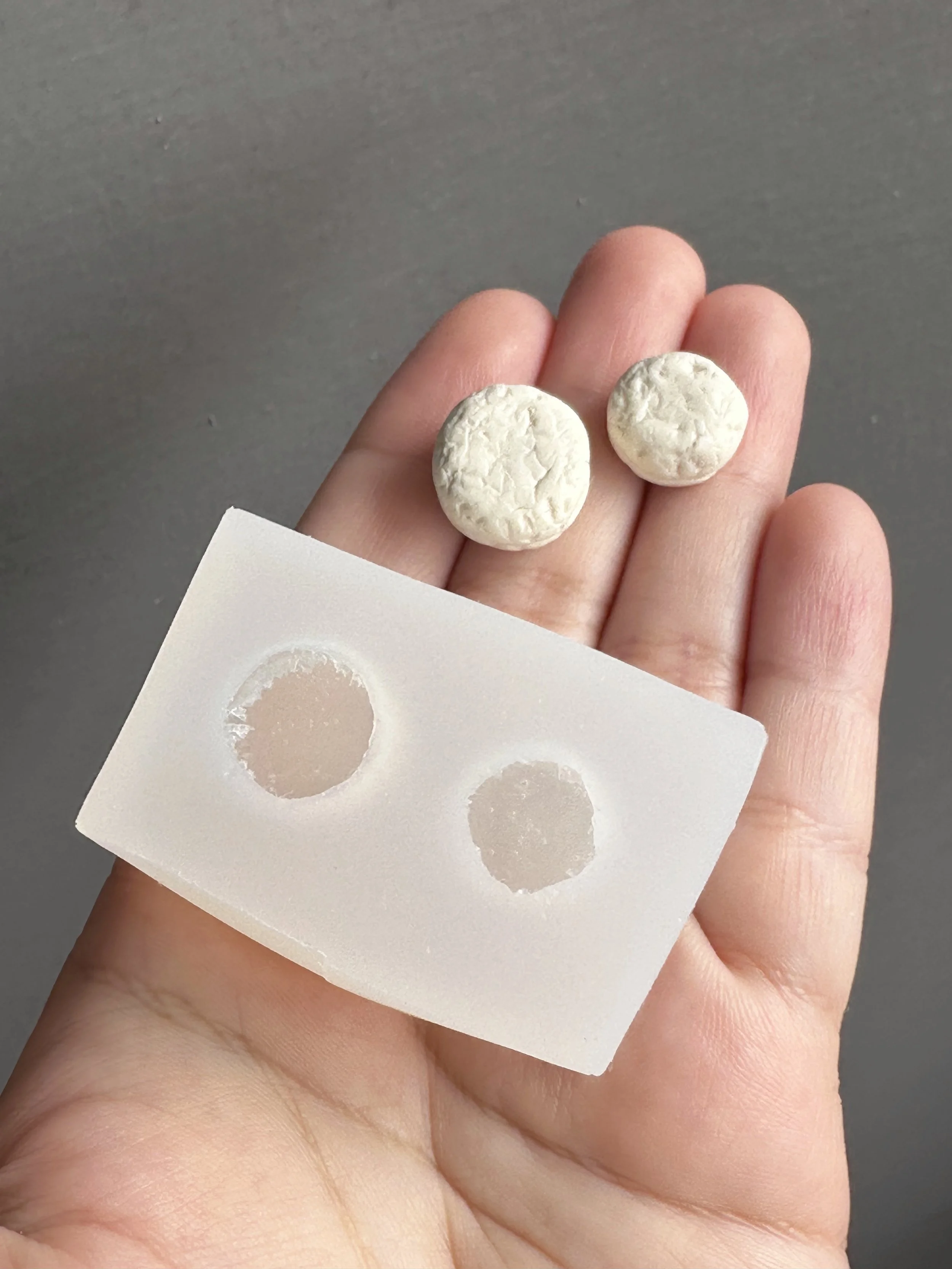 A hand holding a mini biscuits duo silicone mold with the master copies next to it.