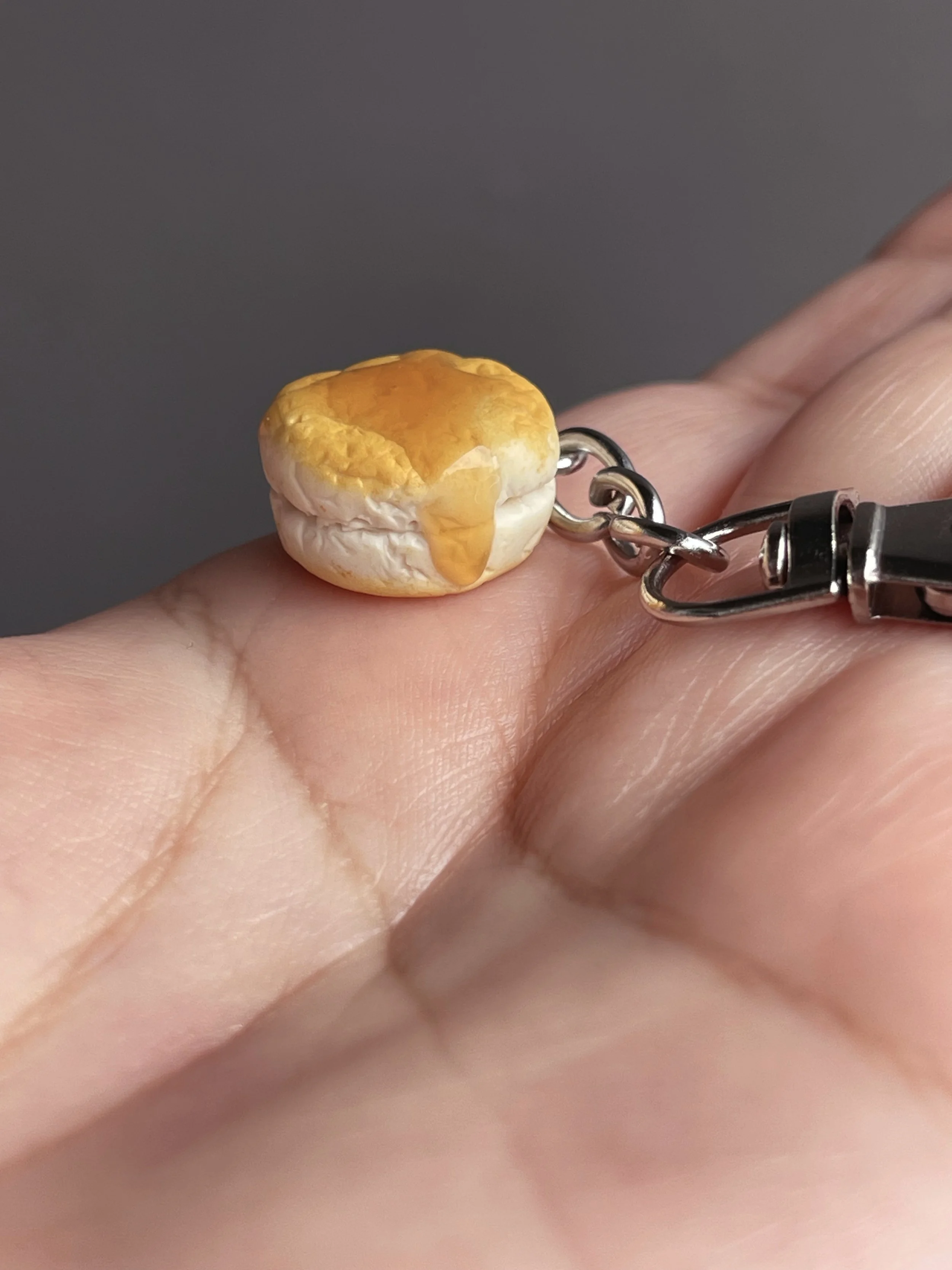 A hand holding a mini polymer clay biscuit and honey keychain.