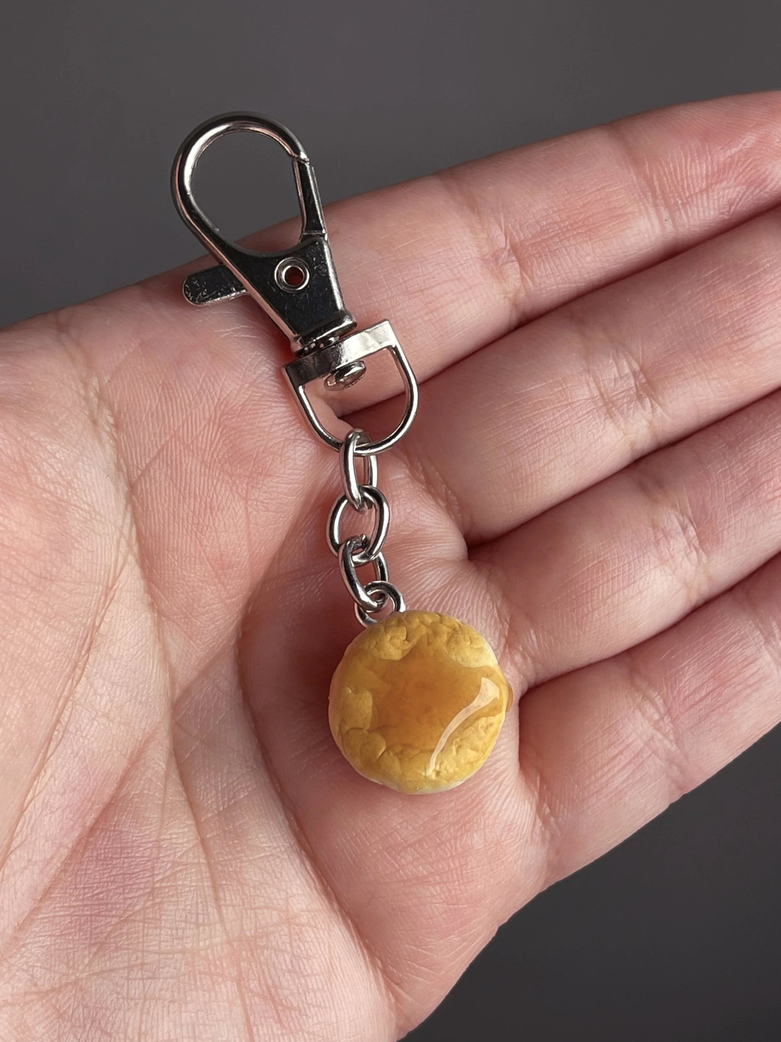 A hand holding a mini polymer clay biscuit and honey keychain.