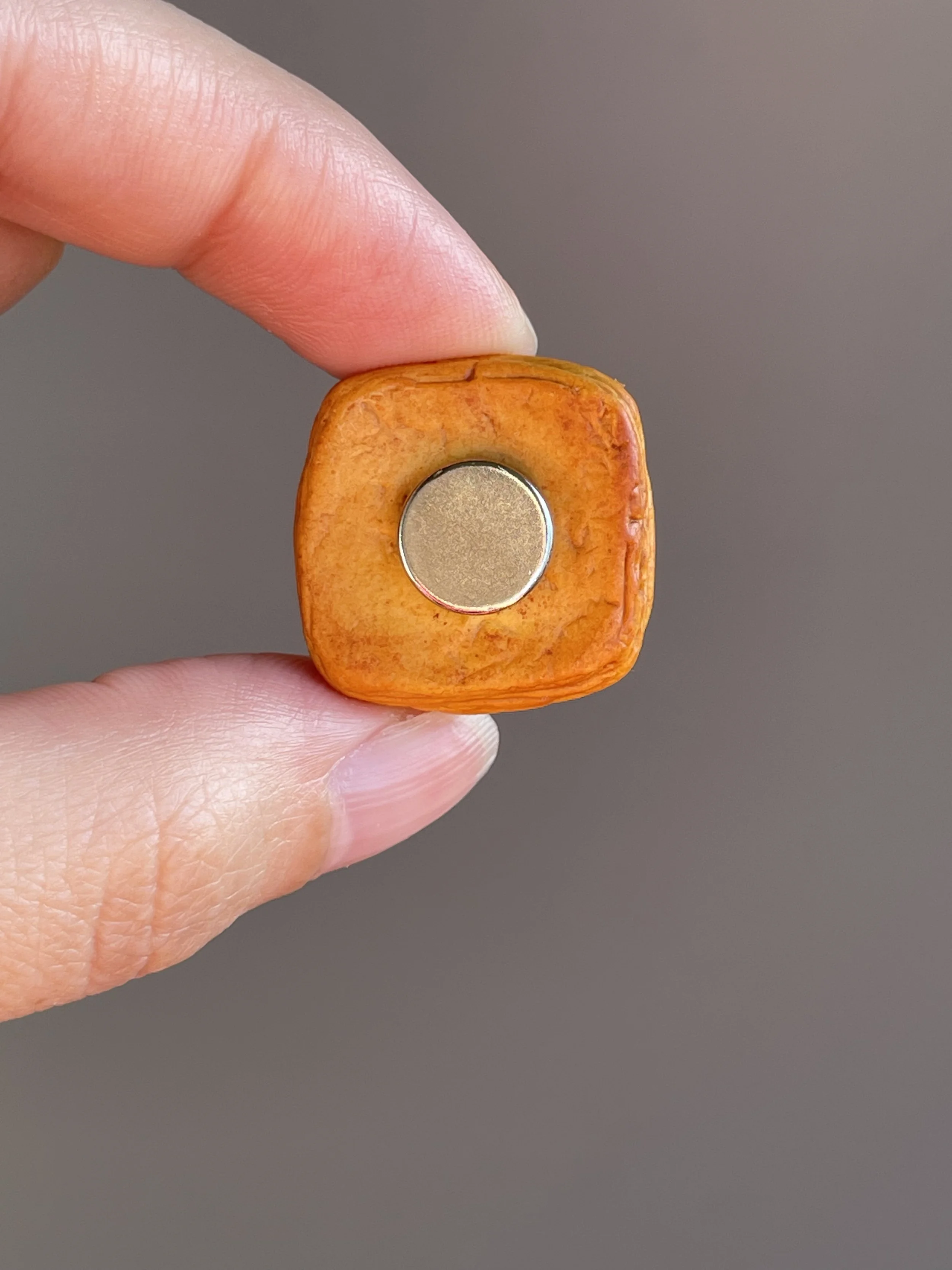 Fingers holding a miniature polymer clay egg danish magnet with runny egg yolk showing the back.