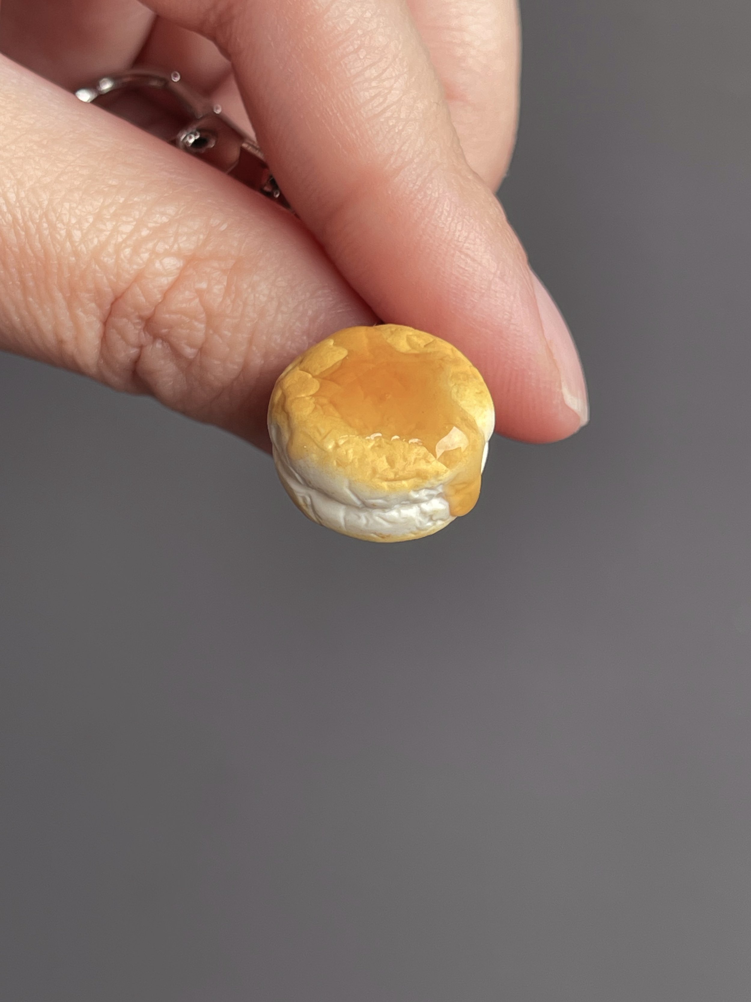Fingers holding a mini polymer clay biscuit and honey keychain.