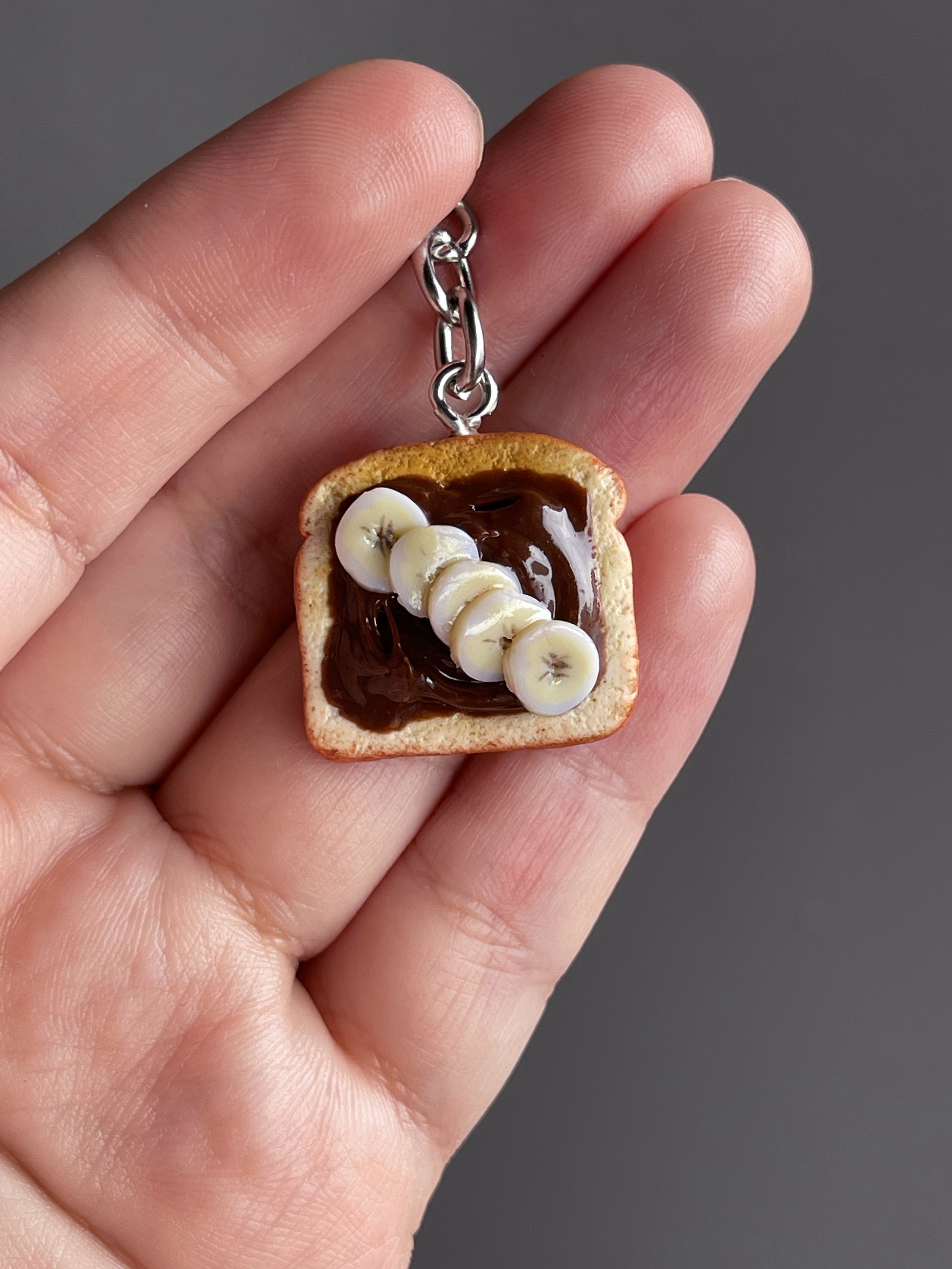 A hand holding a miniature polymer clay toast with hazelnut spread and banana slices.