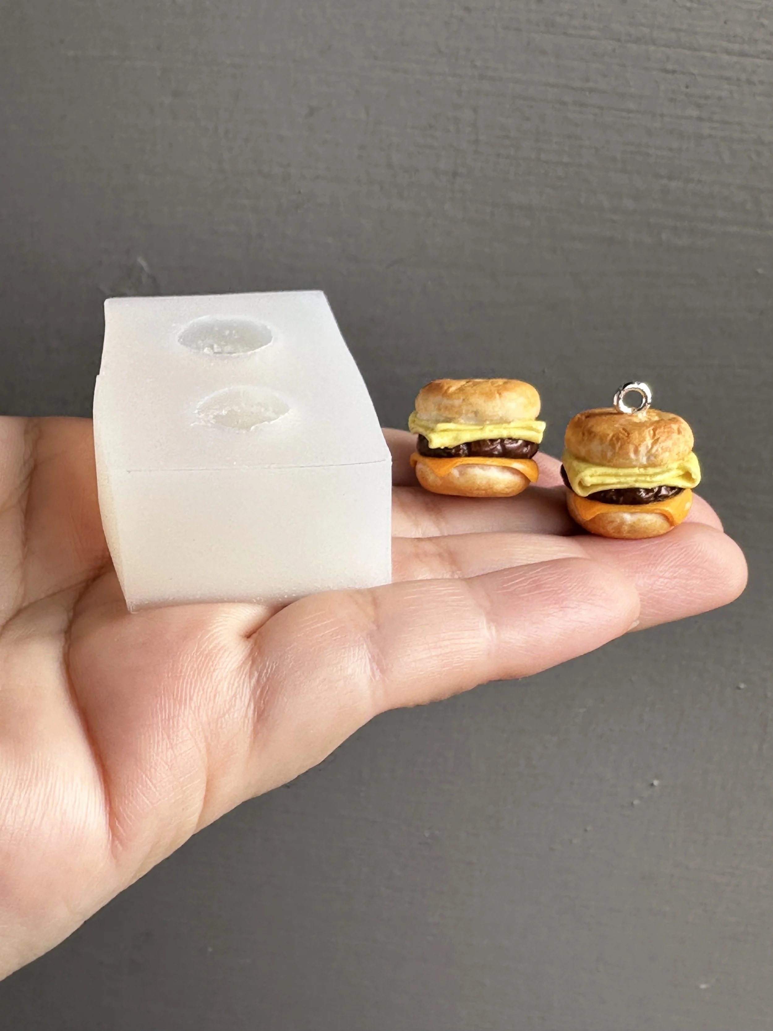 A hand holding a mini biscuits duo silicone mold with samples of the types of biscuits that can be made from the mold.