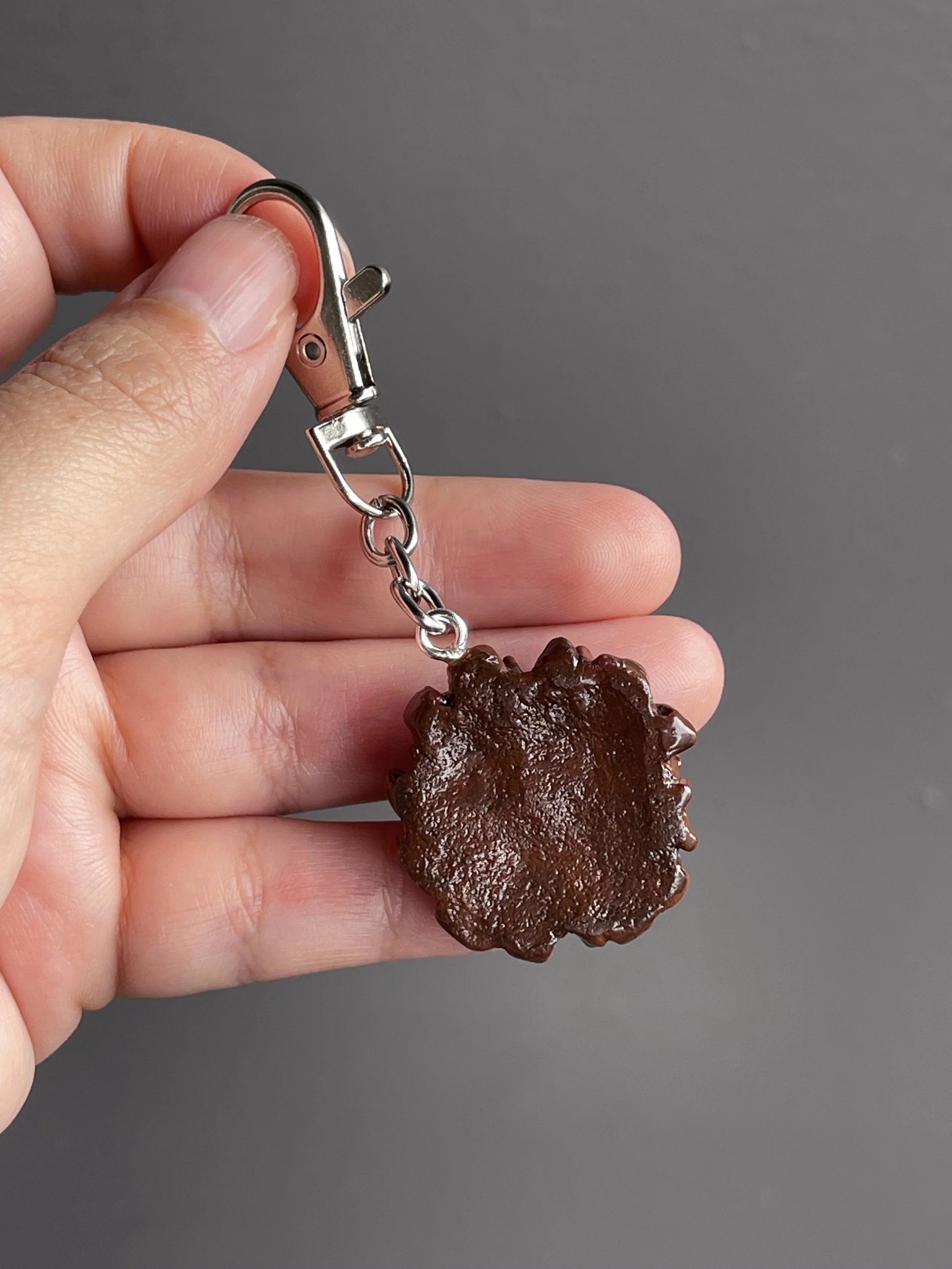 A hand holding a miniature polymer clay chocolate waffle keychain with strawberry slices & ice cream toppings showing the back of the piece.