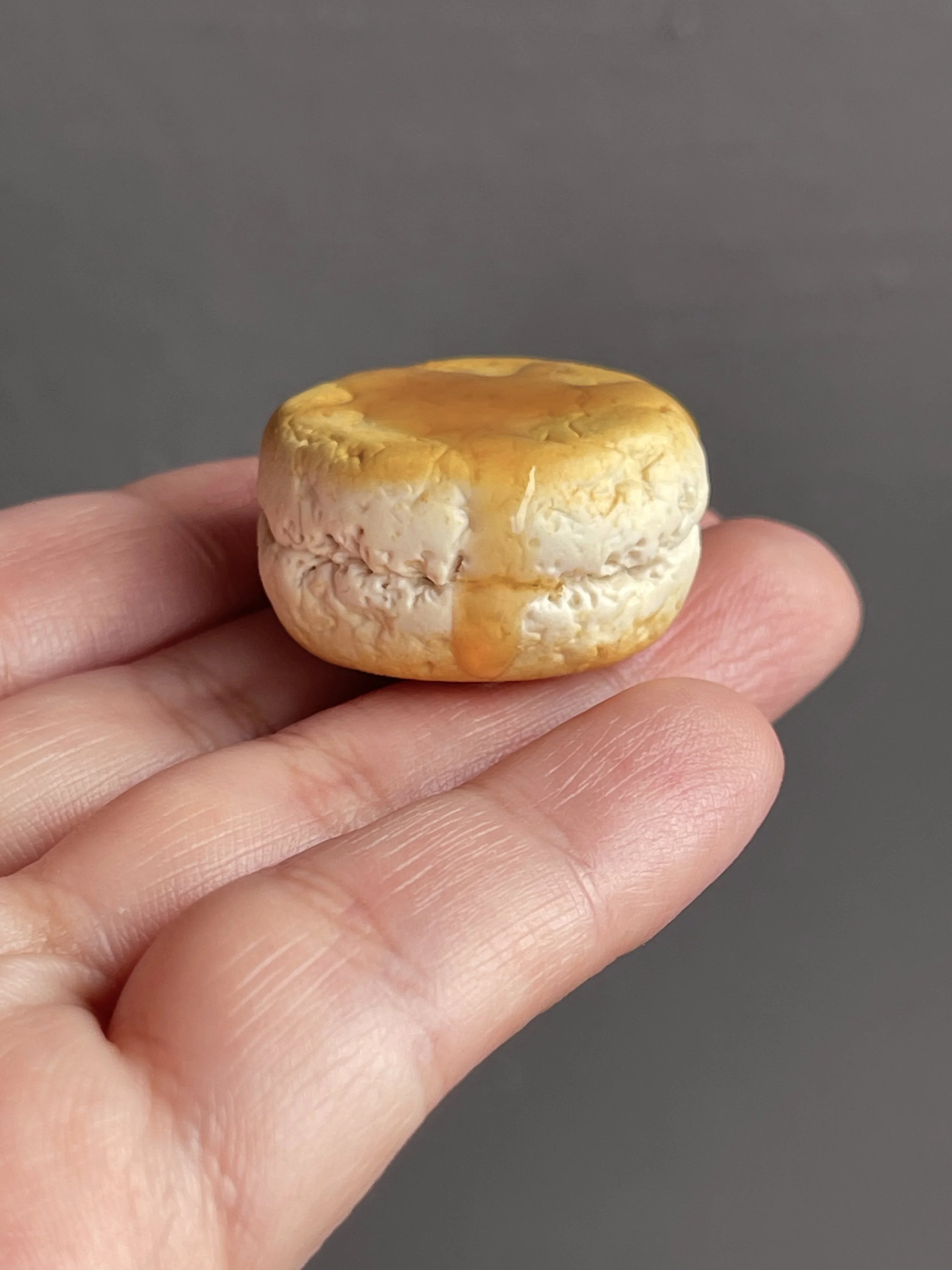 A hand holding a polymer clay biscuit and honey magnet.