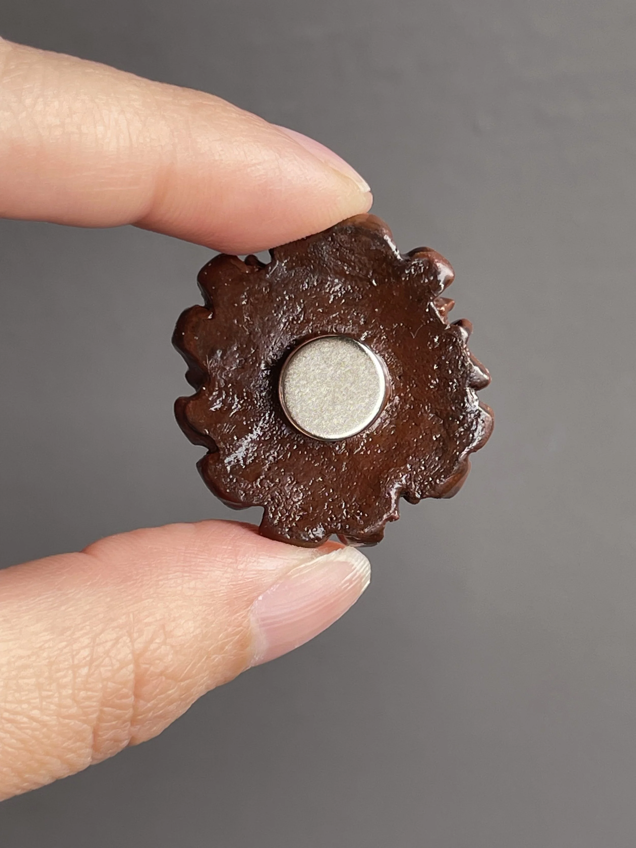 Fingers holding a miniature polymer clay chocolate waffle magnet topped with strawberries and whipped cream showing the back.