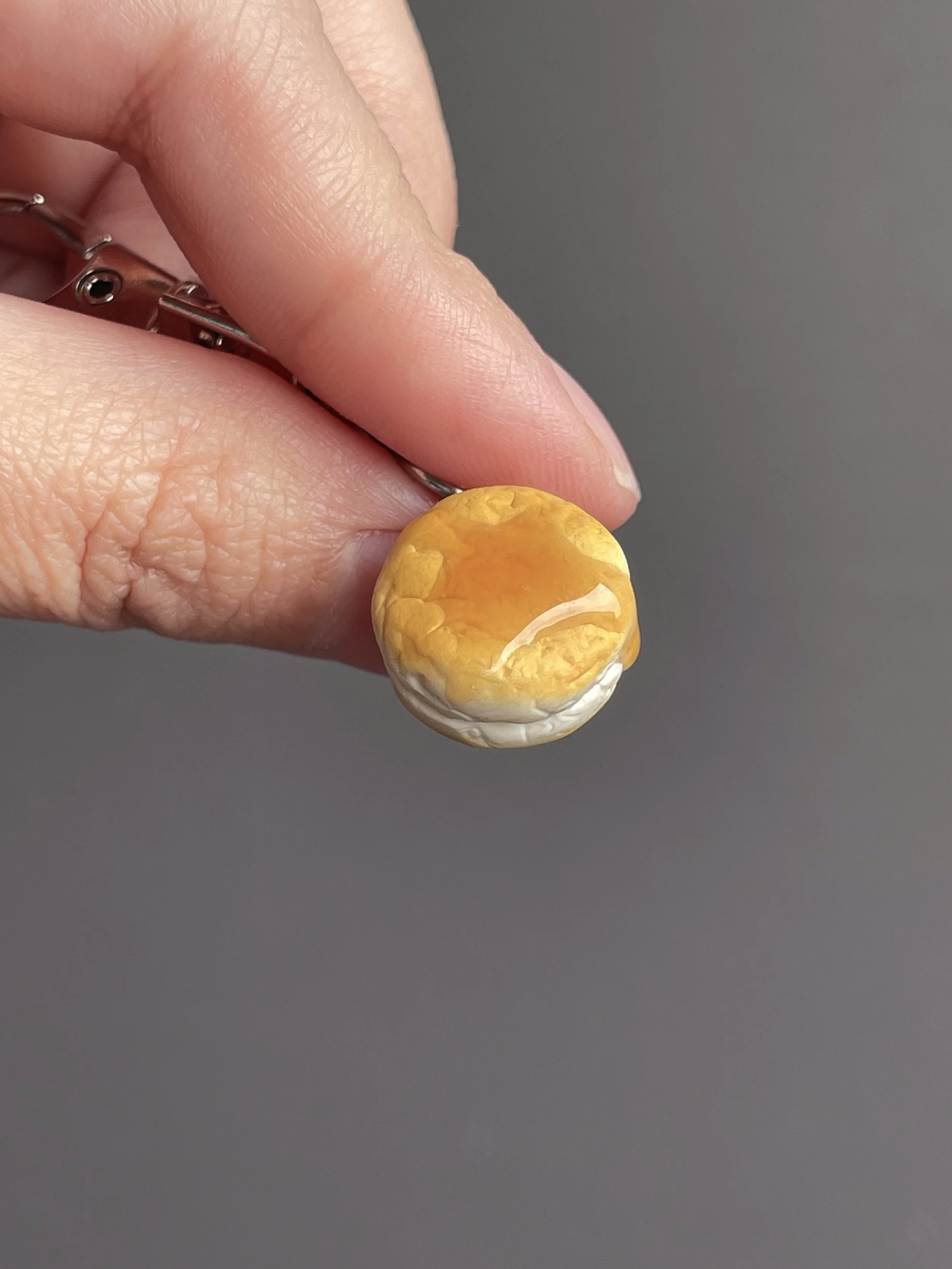 Fingers holding a mini polymer clay biscuit and honey keychain.